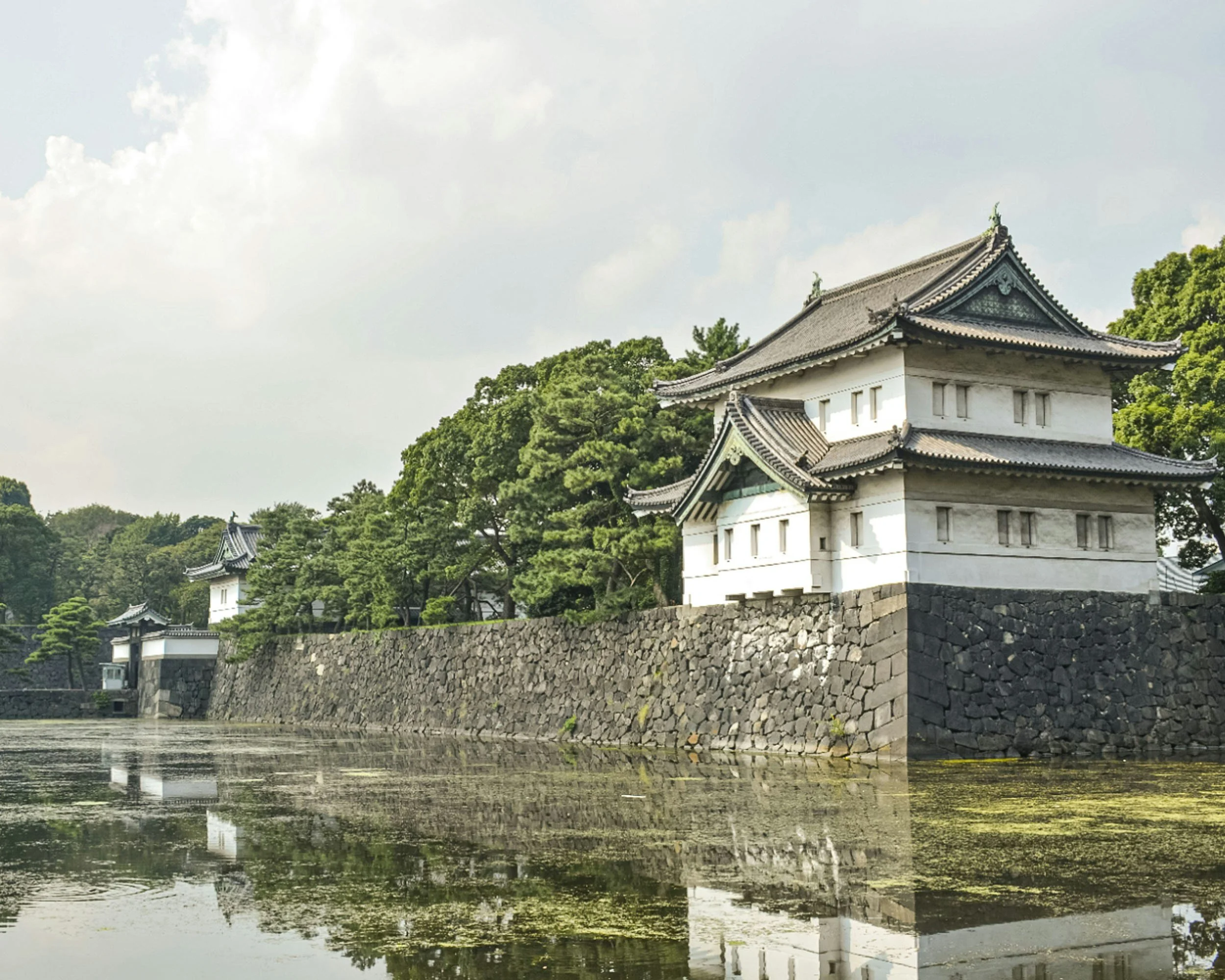 The Fujimi-yagura watchtower of the Imperial Palace in Tokyo reflected in the moat, surrounded by lush pine trees in summer