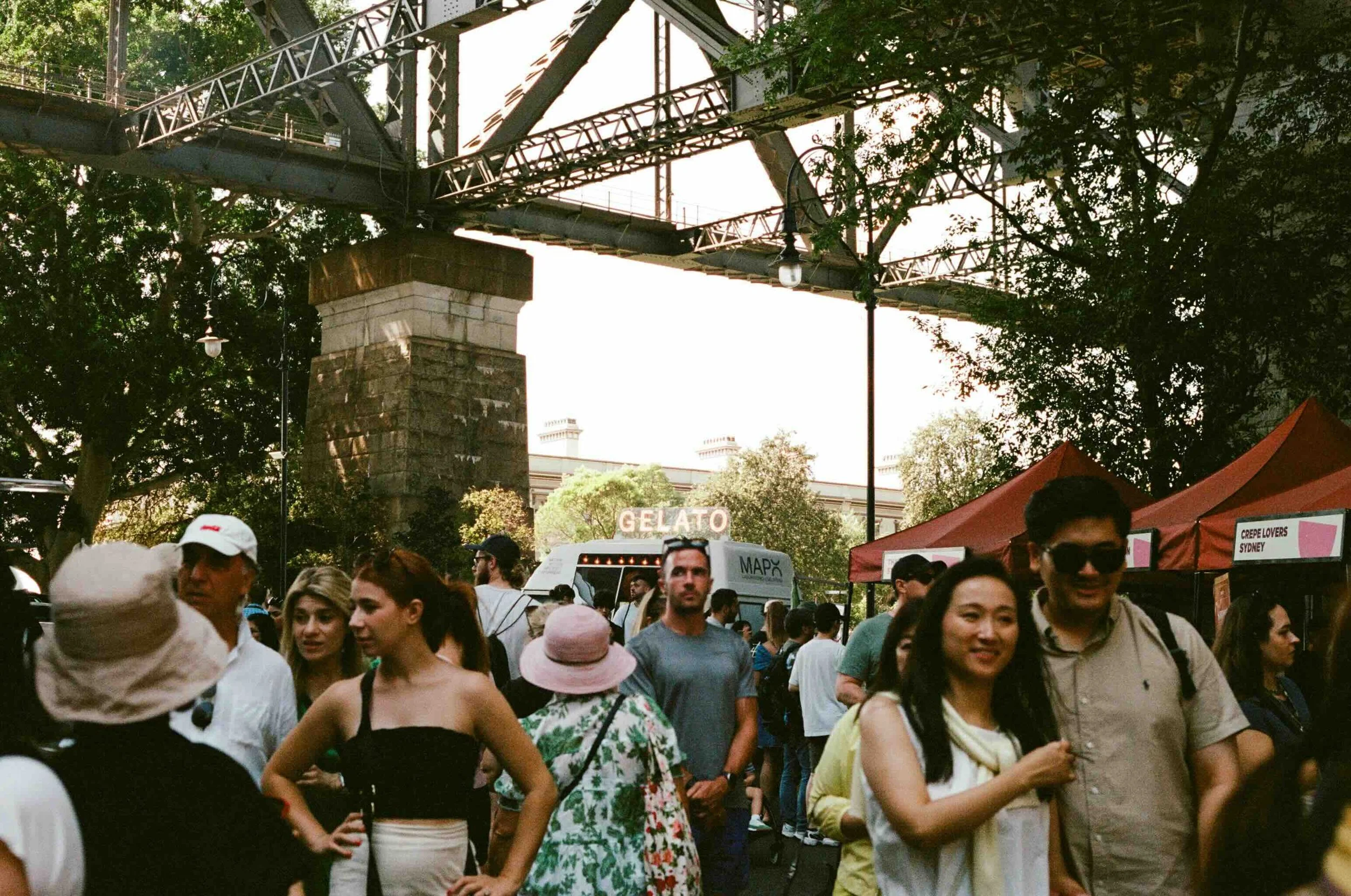historic The Rocks- A bustling Sydney street market beneath a heritage railway bridge, with food stalls and diverse crowds — a cultural immersion experience on Libertas Travel's Sydney high school excursions.