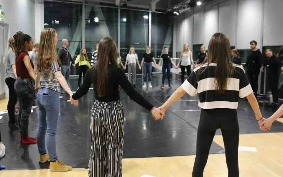 High school drama students standing in a circle holding hands during a professional theatre workshop at The Lowry, Salford — a transformative Performing Arts experience on a Libertas Travel school tour.