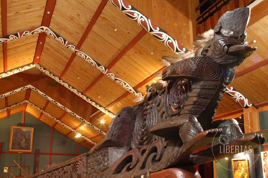 Maori culture indigenous tribal Whanganui boat carved from wood sits within a museum constructed of wood and decorated with painted beams
