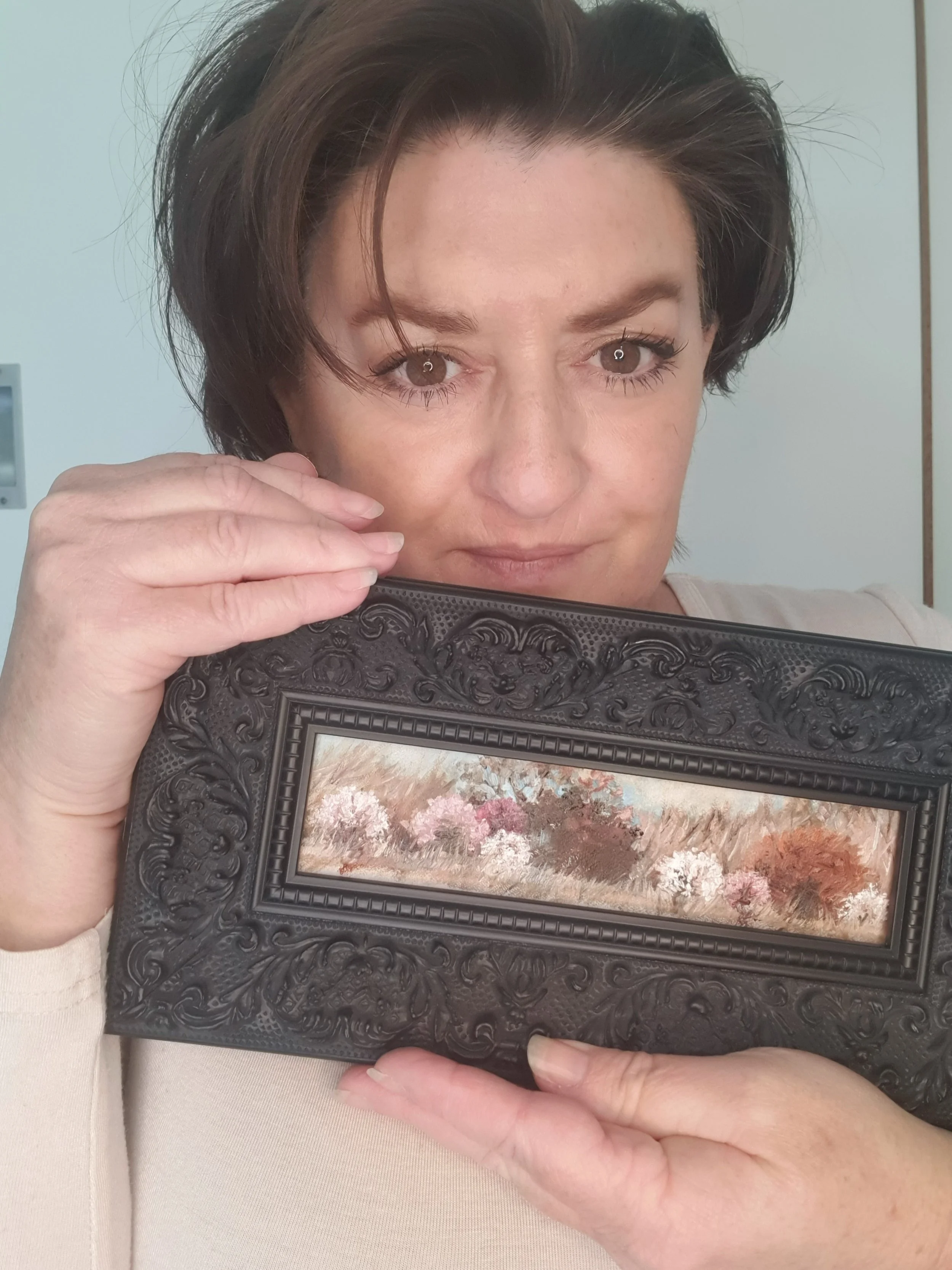 Australian artist Victoria Pynt holding miniature oil painting in black ornate frame.