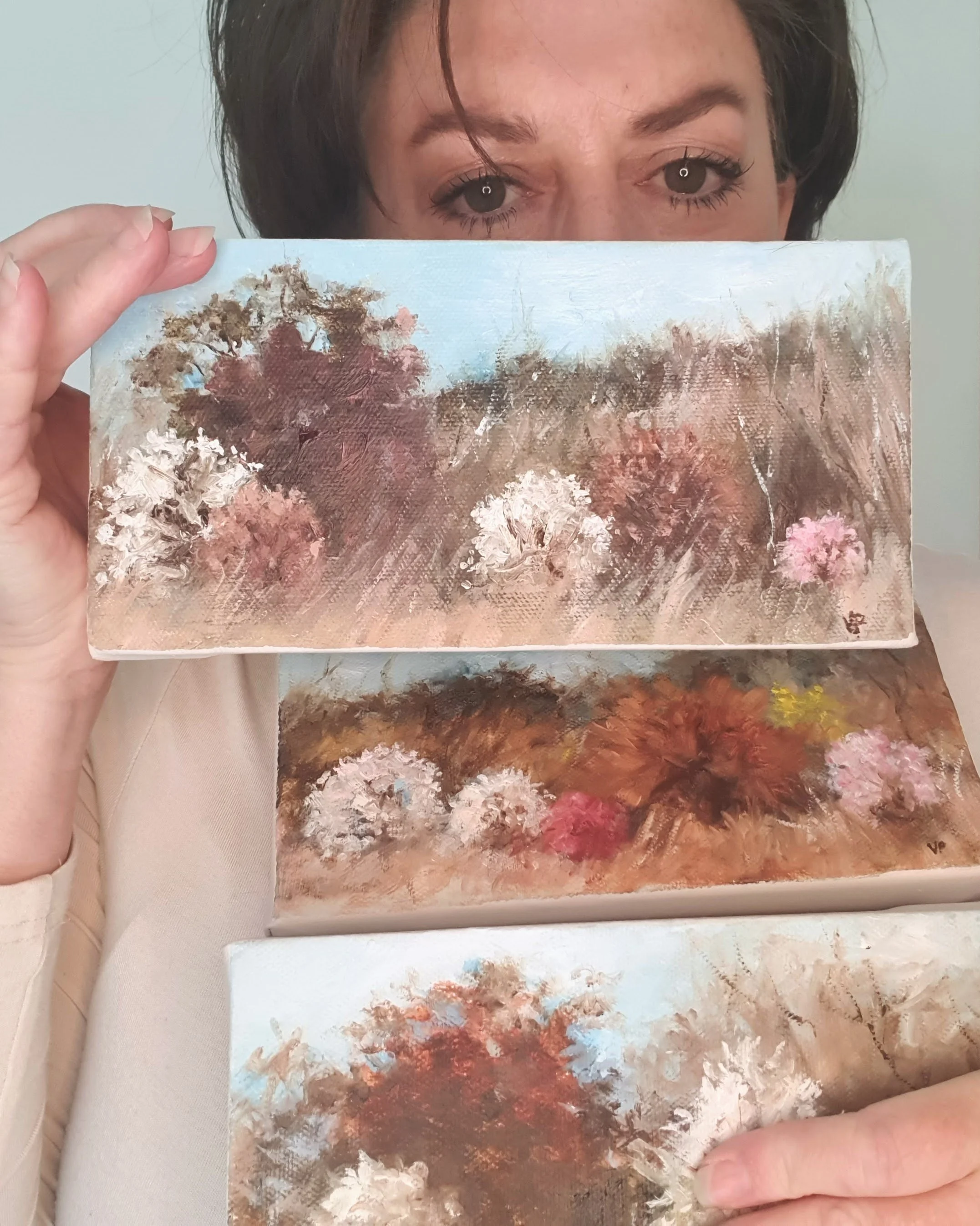 Canberra artist Victoria Pynt holding mini oil paintings. Soft abstract landscape in natural earth tones of light brown and white with cherry blossom.
