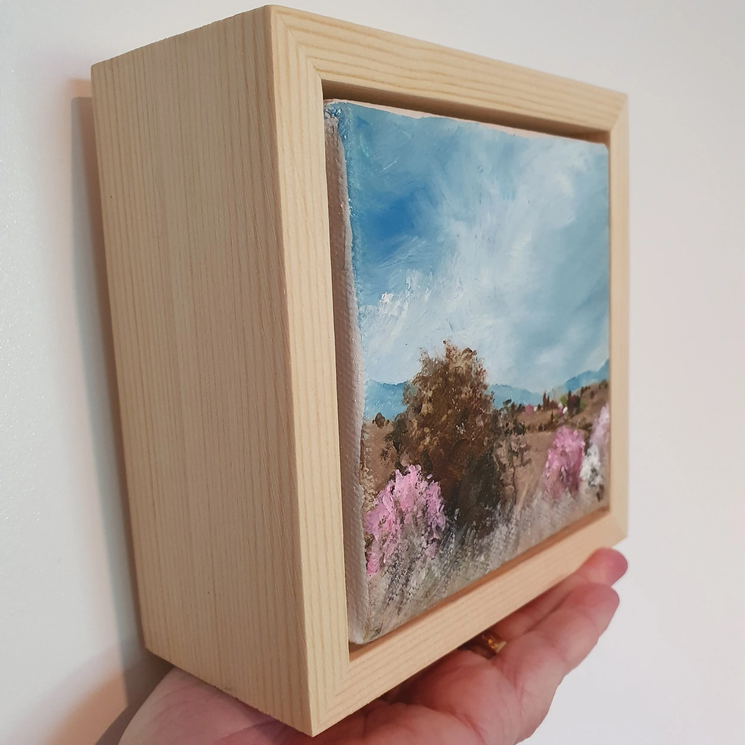 Mini oil painting of country landscape in natural earth tones of light brown and white with pink cherry blossom.