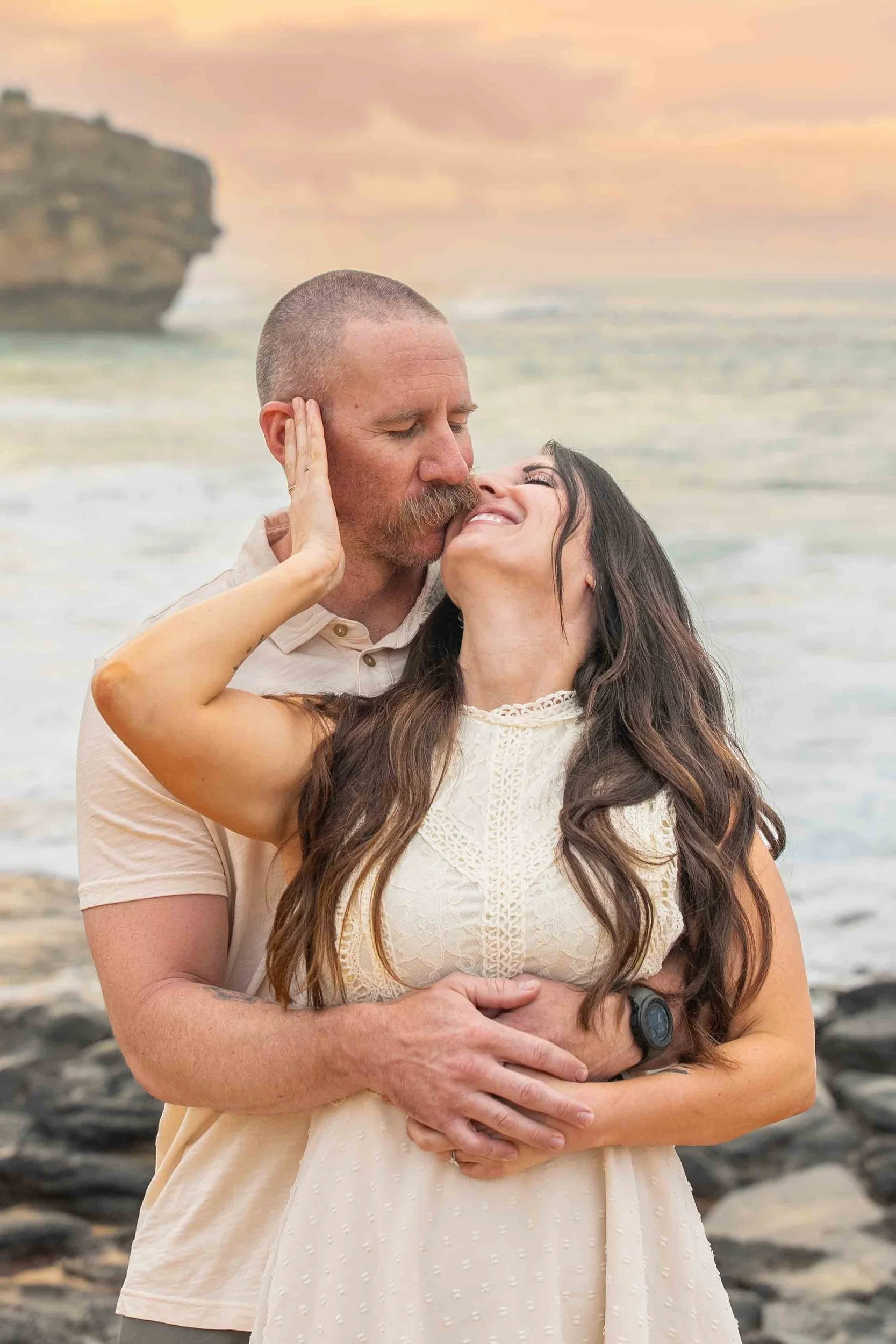 Couple sharing a tender embrace on the rocky shore at Shipwreck Beach, Kauai.