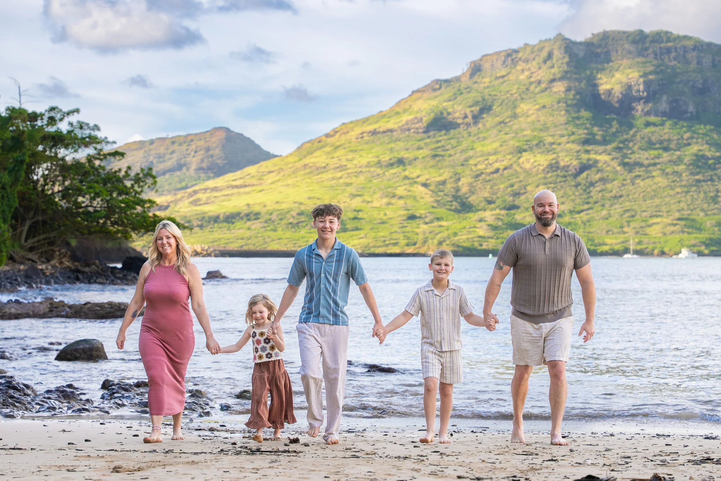 Family of five holding hands while walking along a Kauai shore at golden hour.