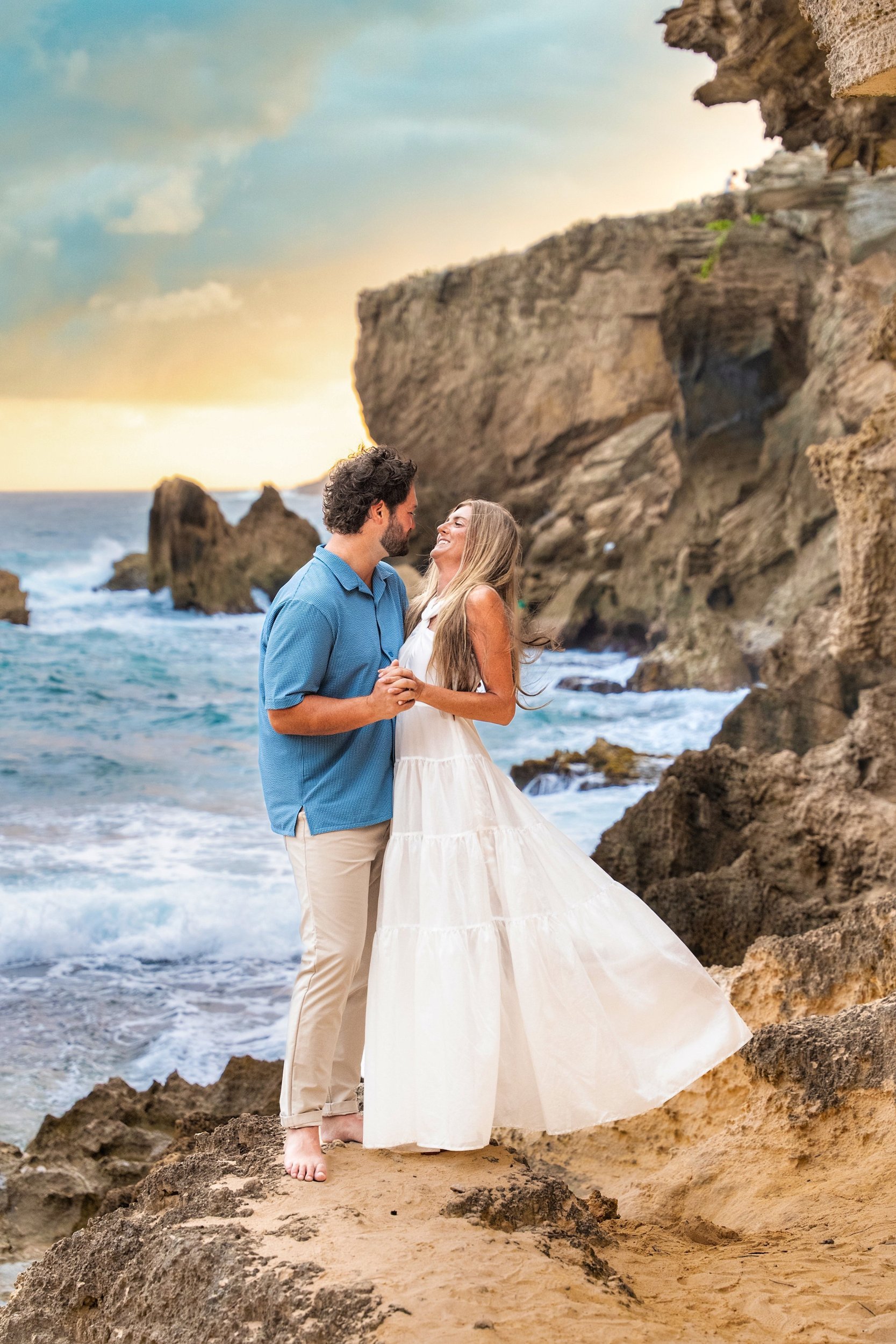 Couple embracing on a rocky cliff at Shipwreck Beach, Kauai, at sunset.