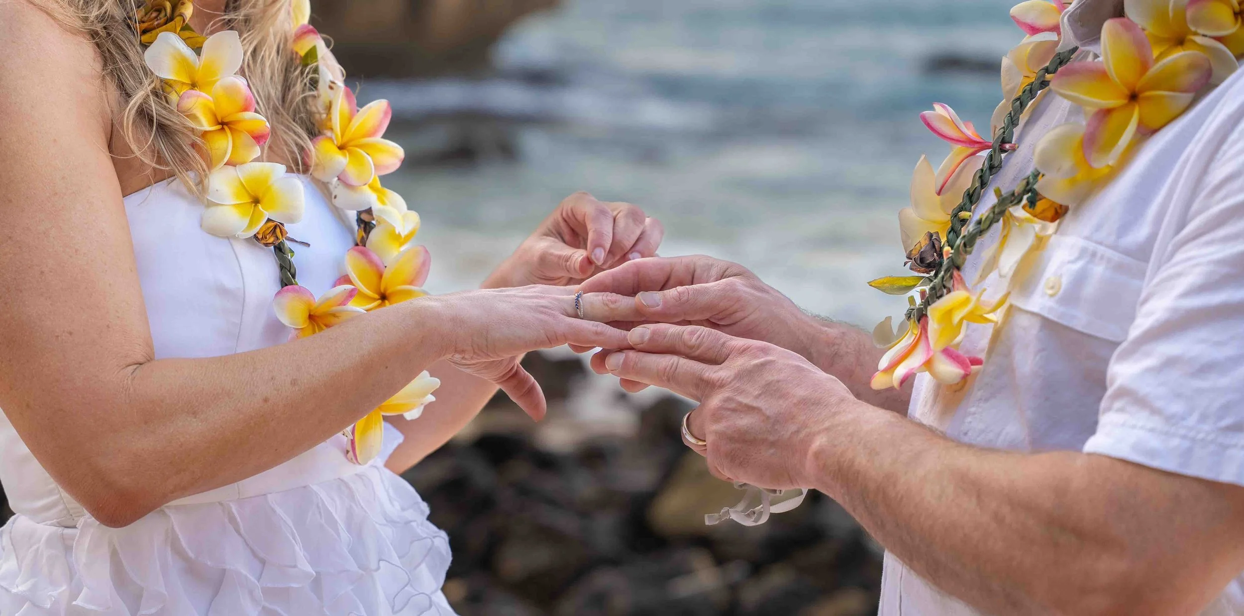 Close-up of a couple exchanging rings while wearing plumeria leis in Kauai.