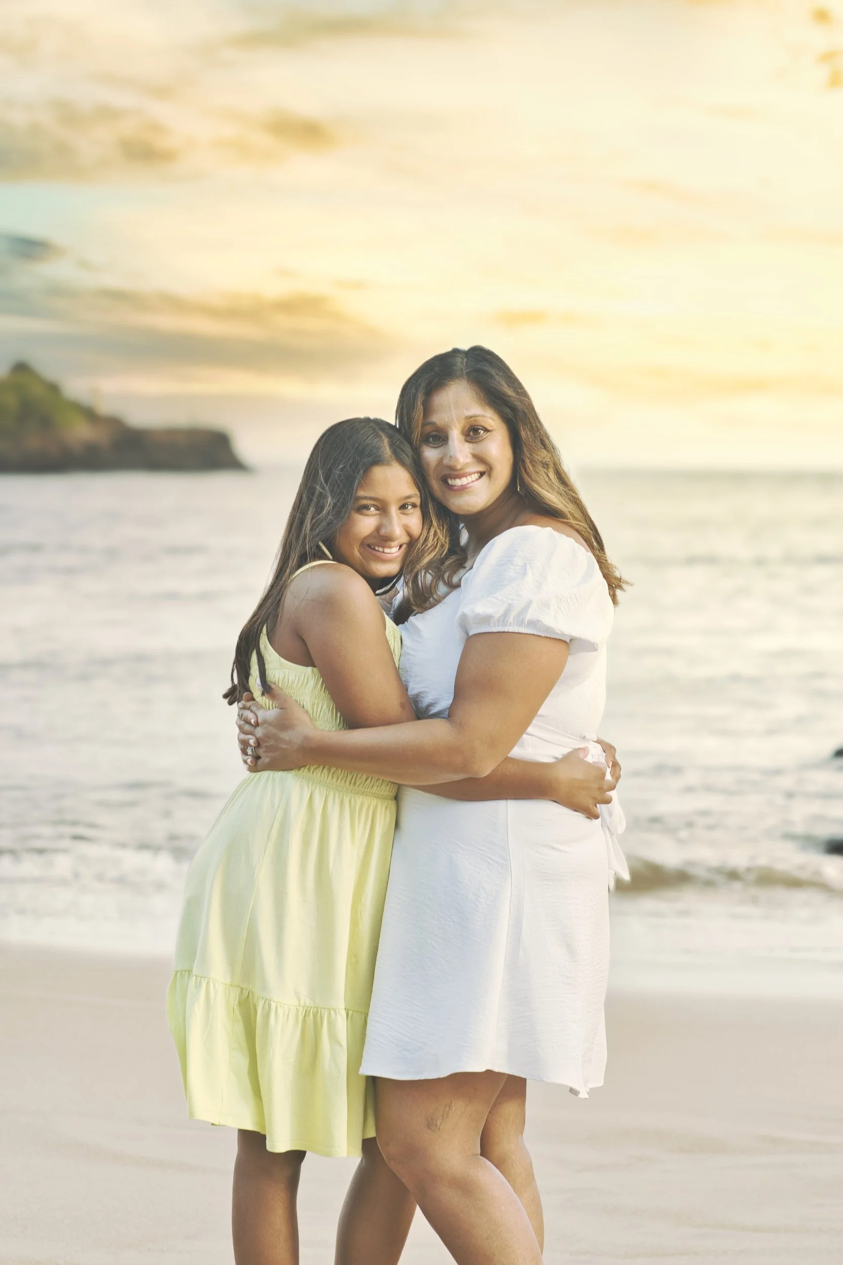 Mother and daughter hugging on a Kauai beach at sunset.
