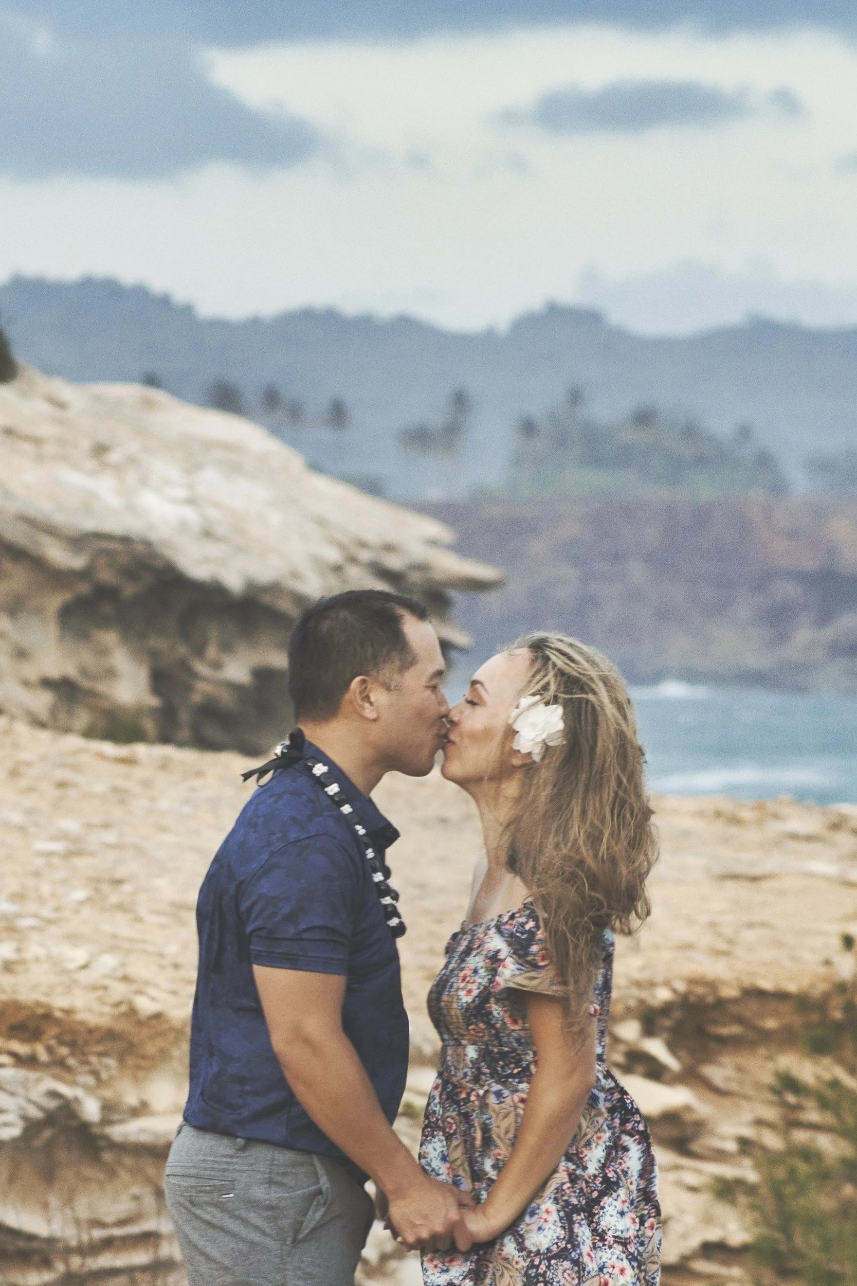 Couple kissing on a cliff top with the ocean stretching behind them at Shipwreck Beach, Kauai.