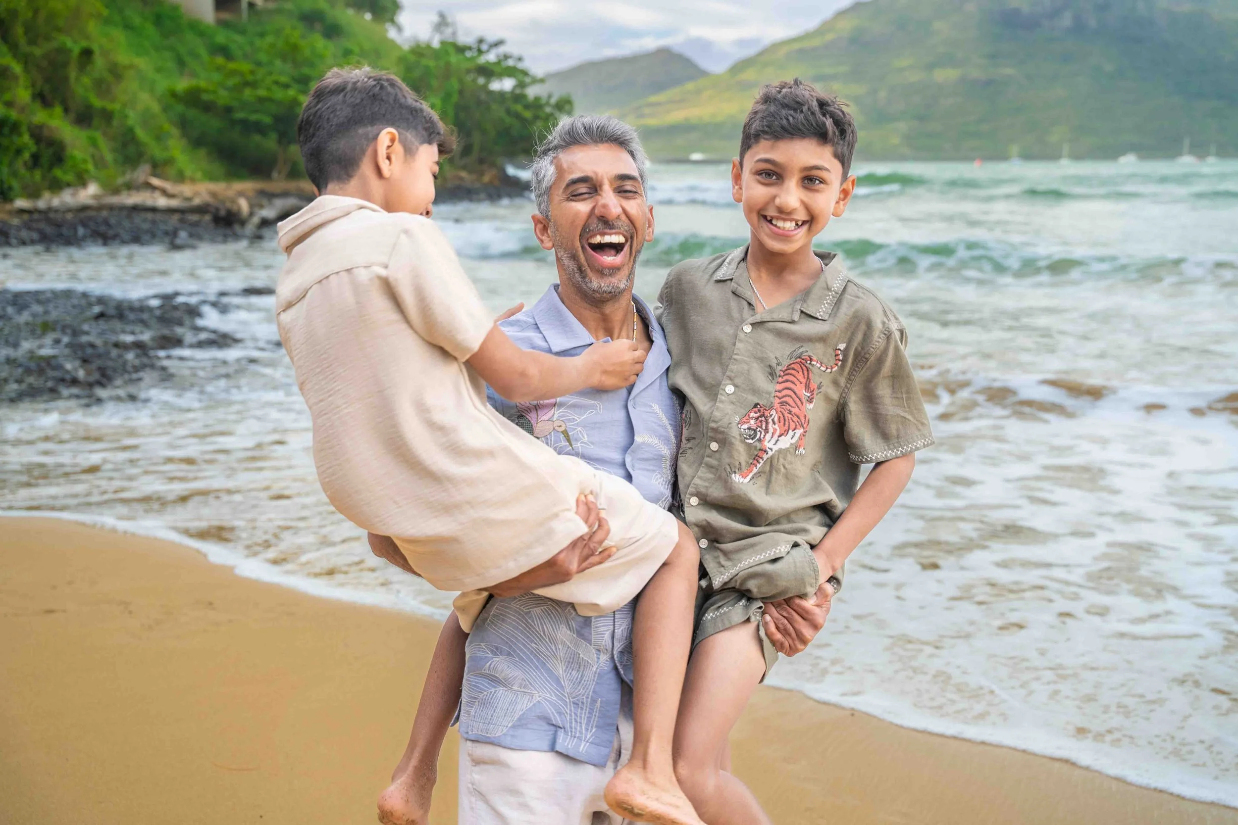 Laughing dad carrying his two sons on a Kauai beach.
