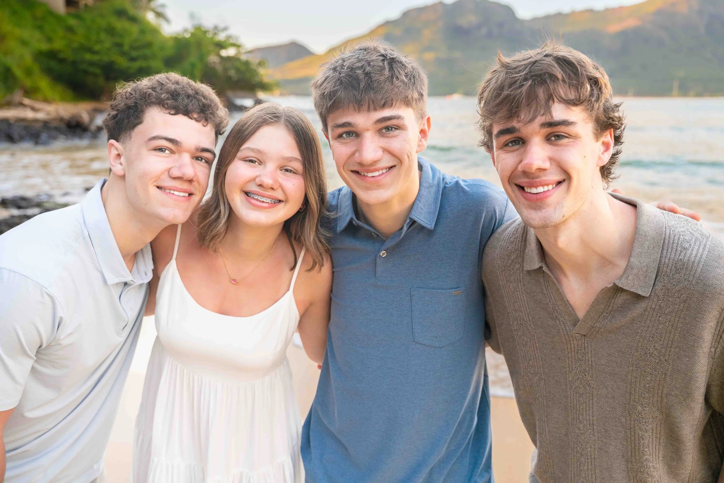 Four smiling siblings posing close together on a Kauai beach.