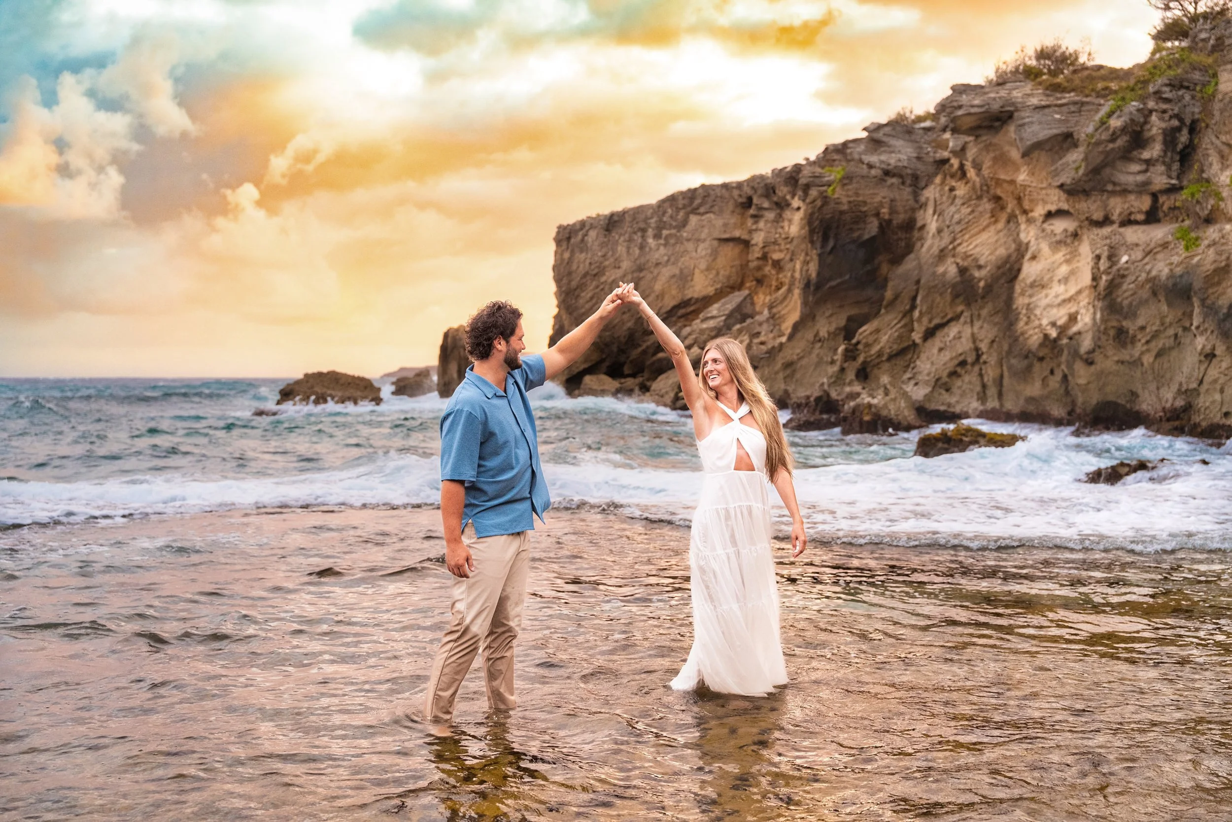Playful newlywed couple dancing in shallow water on a Kauai beach at sunset.