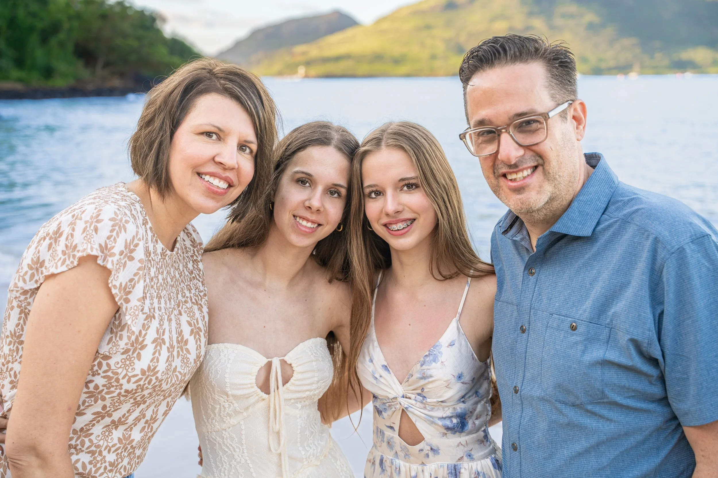 Smiling family of four in a close-up portrait by a Kauai bay.