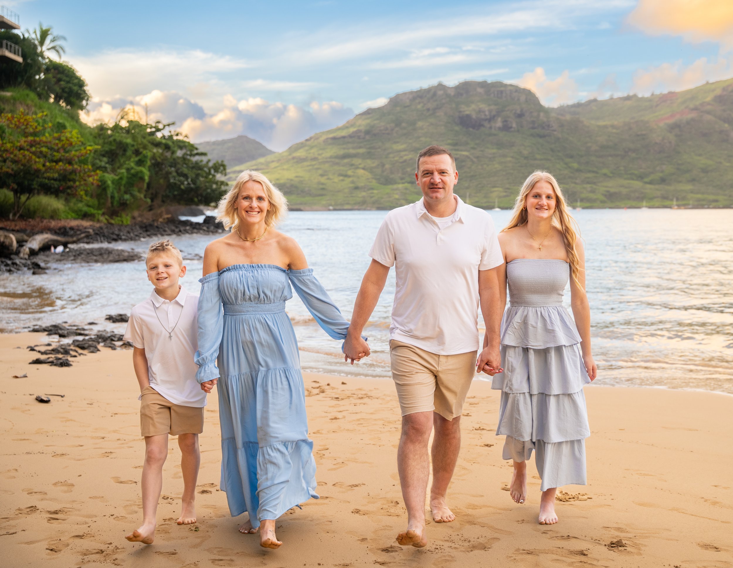 Family of four walking hand in hand along a Kauai beach with mountains behind them.