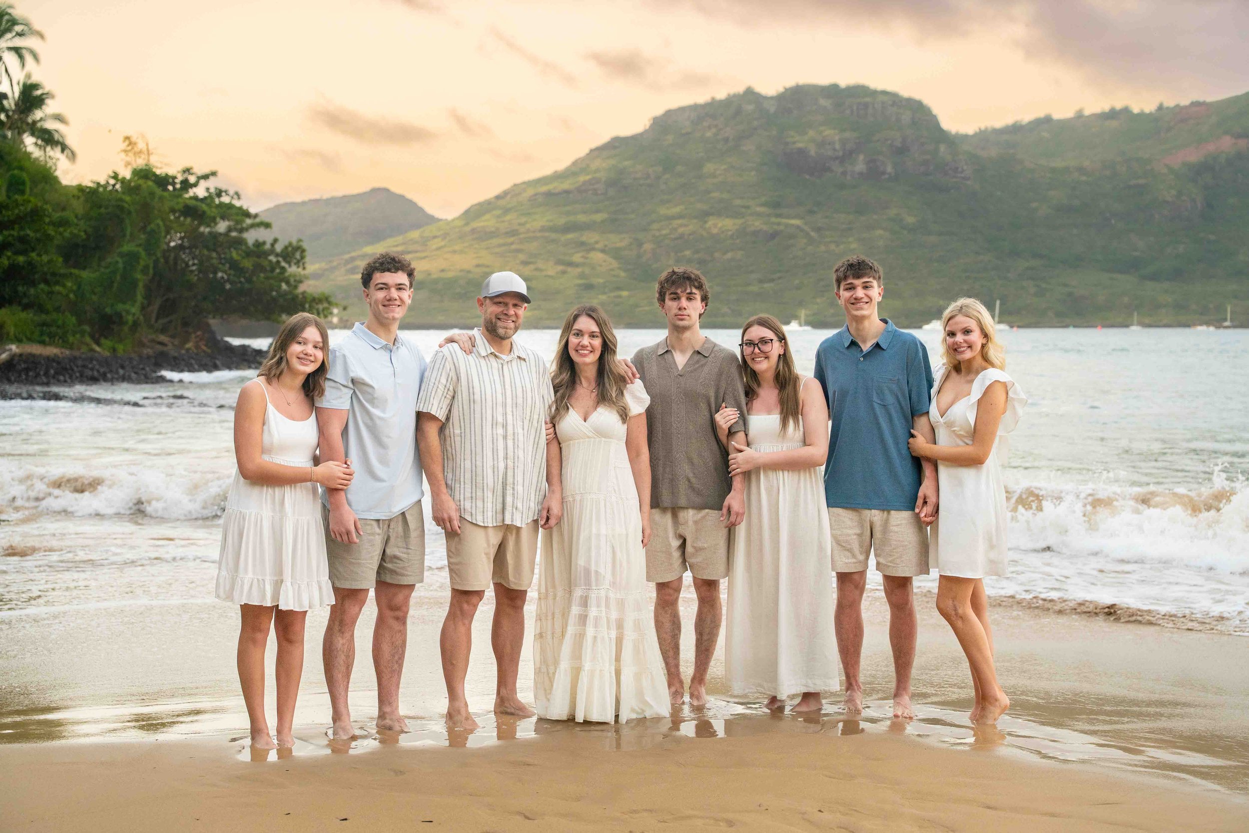 Large extended family standing together on a Kauai beach at sunset.