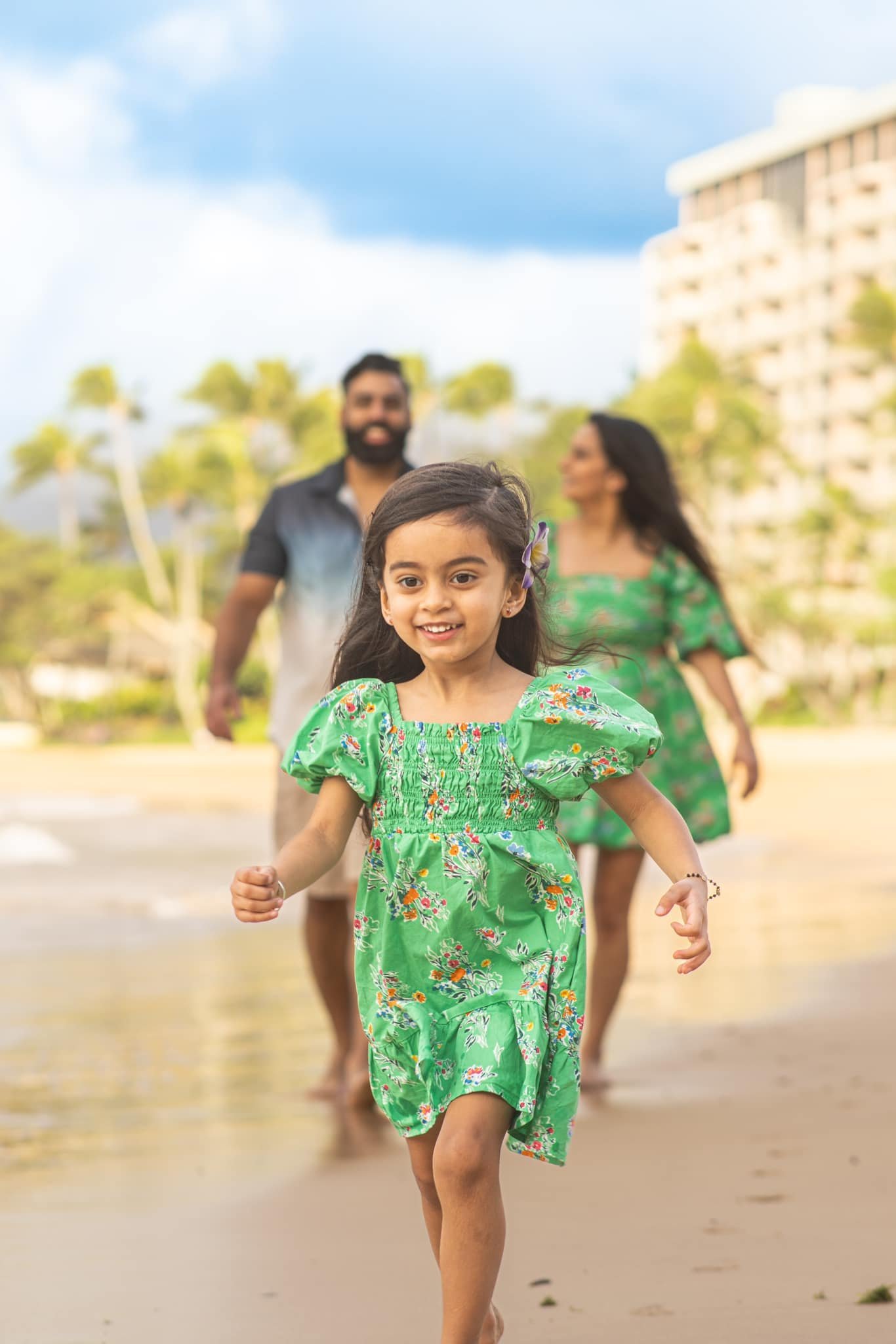 Smiling little girl in a green floral dress running toward the camera on a Kauai beach.