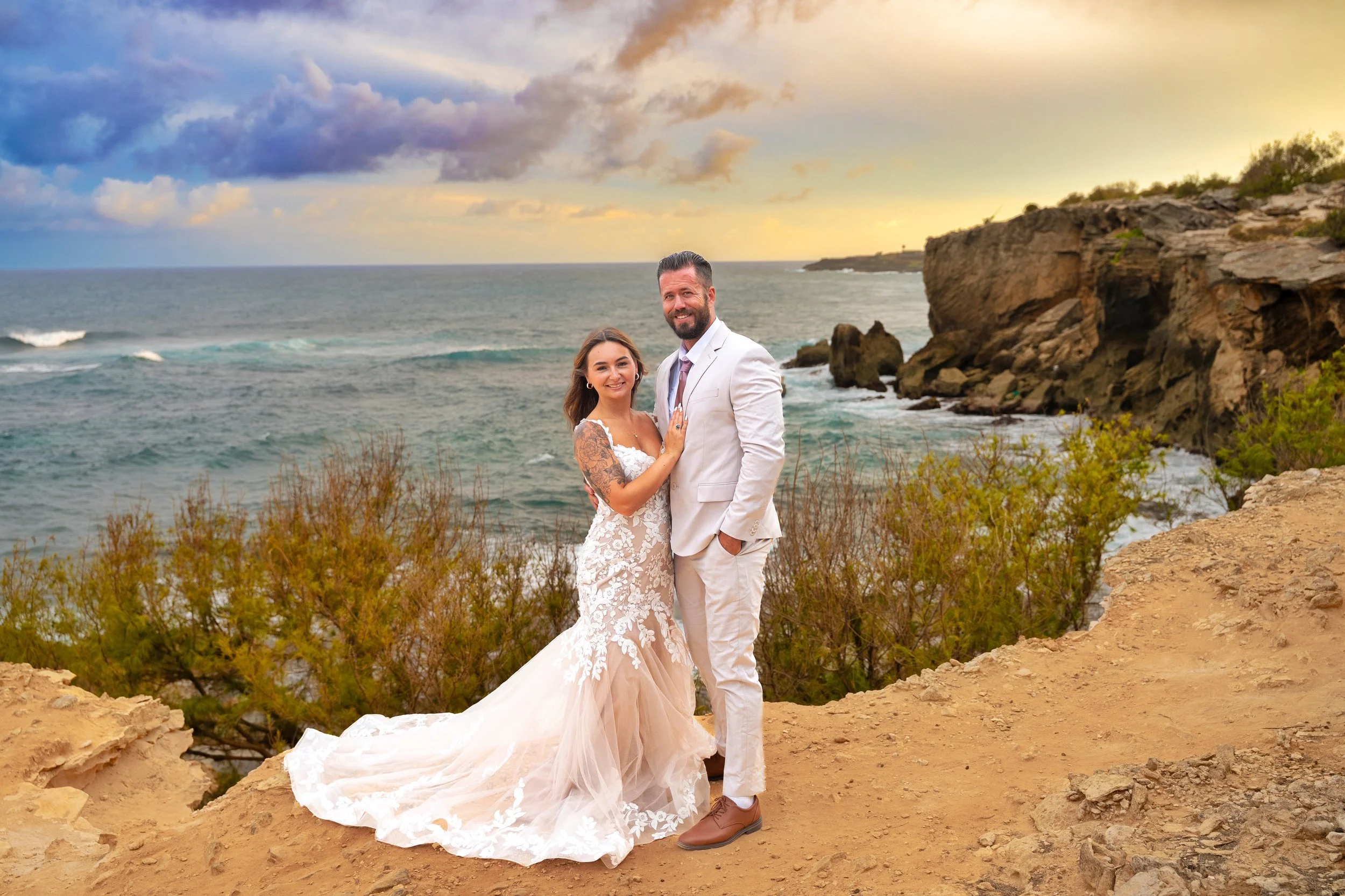 Newlywed couple posing on a cliff top at Shipwreck Beach, Kauai, at sunset.