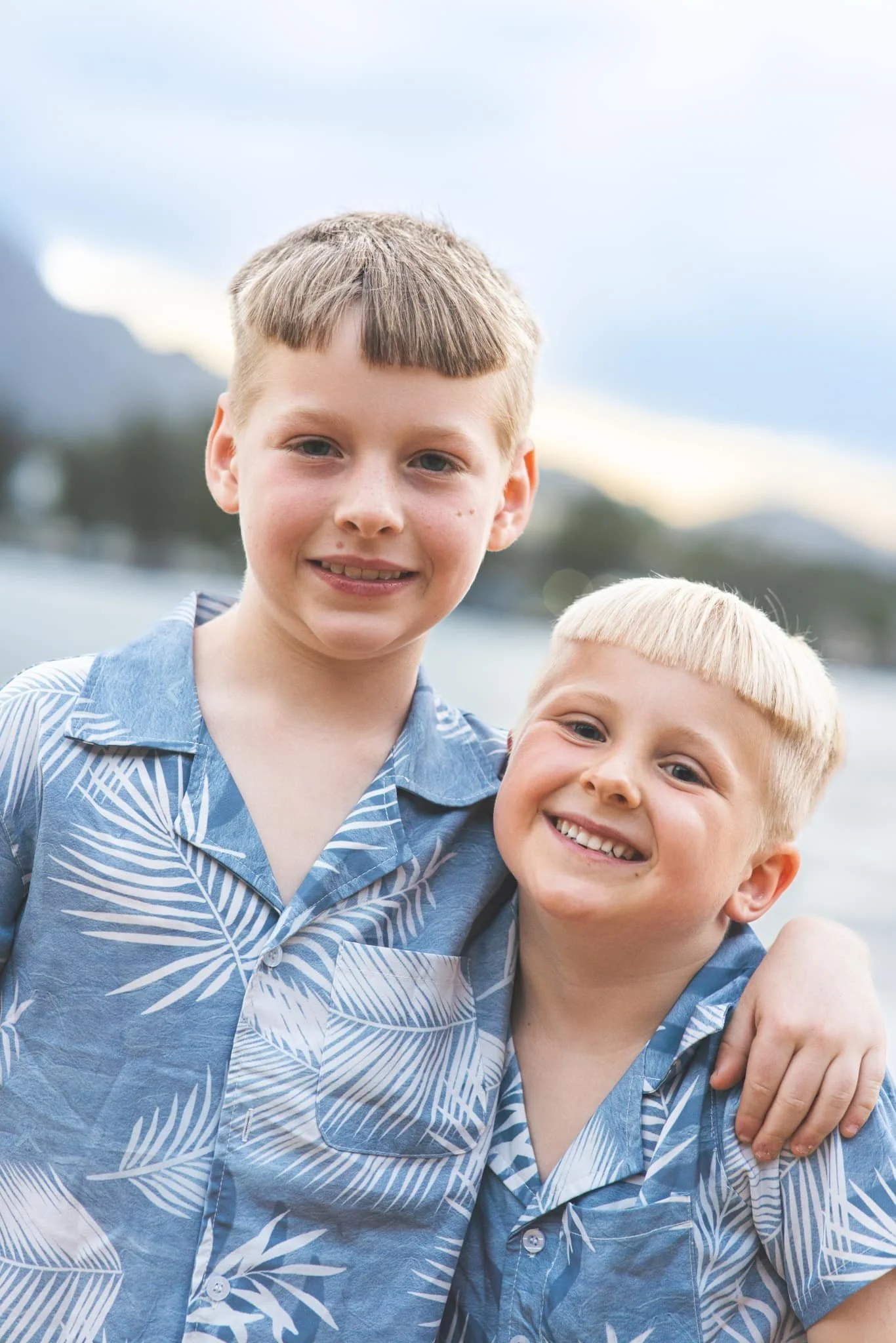 Two young brothers in blue aloha shirts hugging and smiling on a Kauai beach.