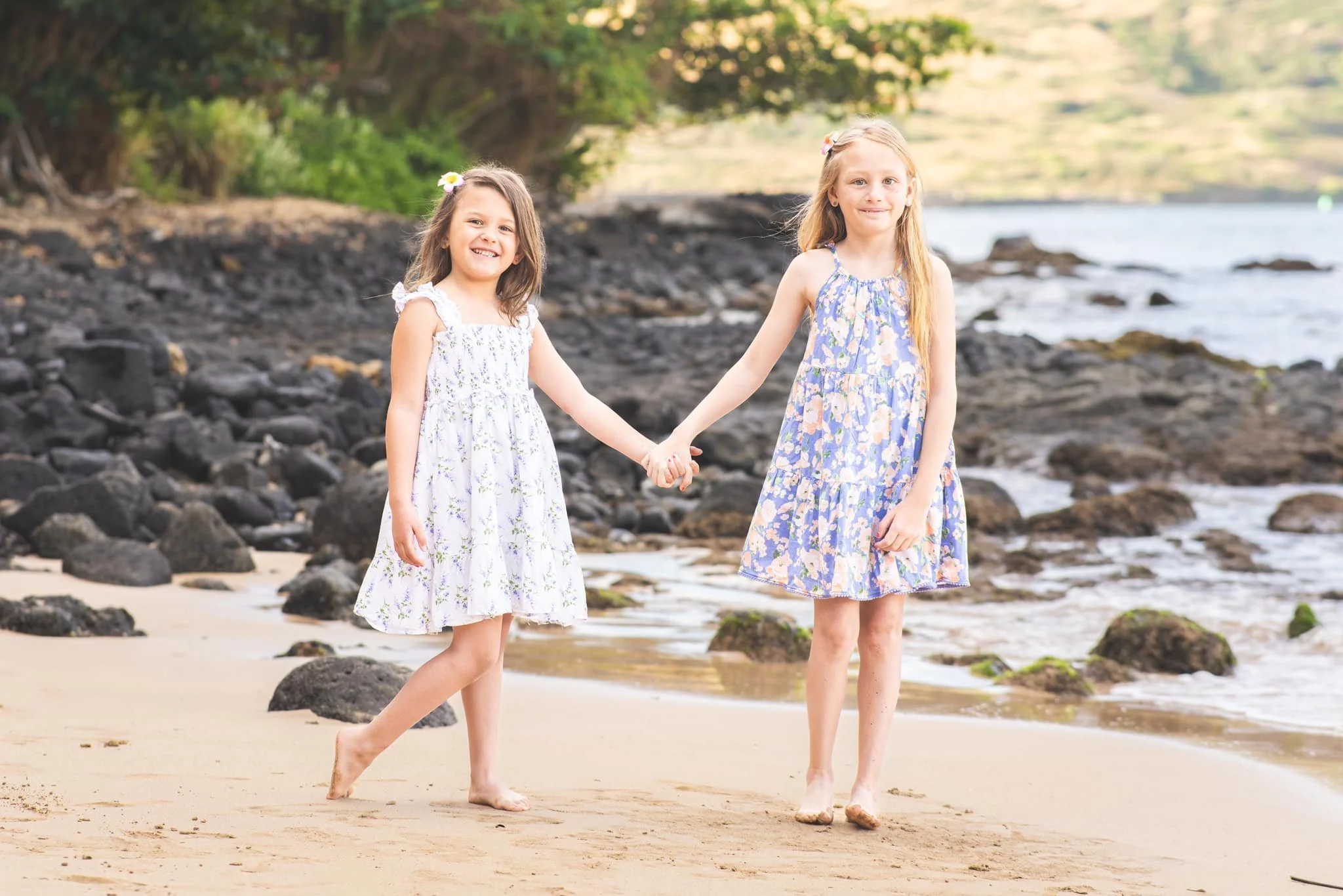 Two young sisters holding hands while posing on a rocky Kauai beach.