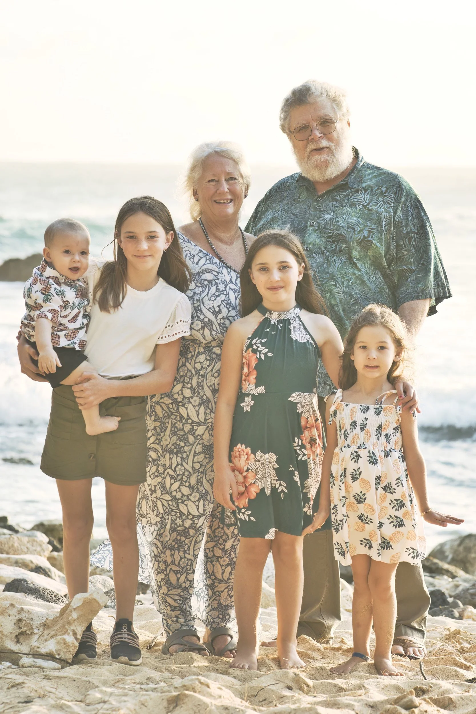 Grandparents posing with their four grandchildren on a Kauai beach at sunset.