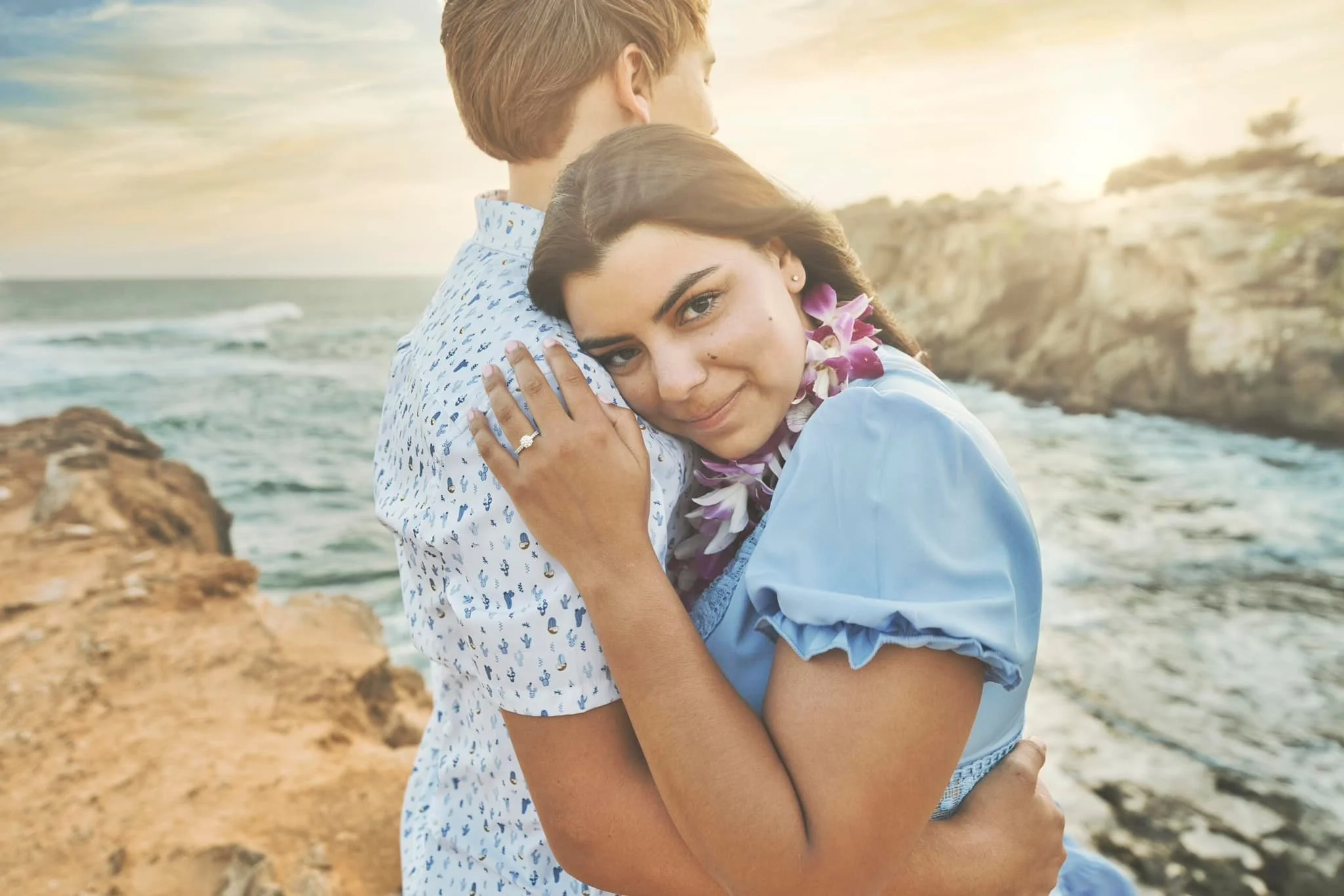 Woman wearing a lei hugging her partner from behind at Shipwreck Beach, Kauai.