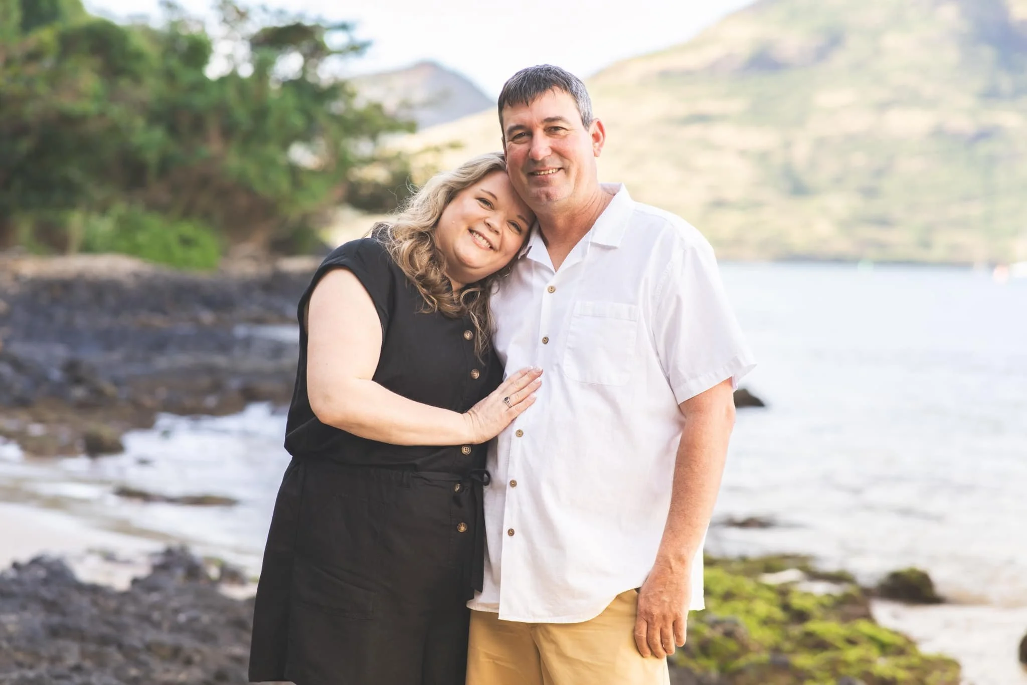 Woman leaning on her partner's shoulder on a rocky Kauai shoreline.