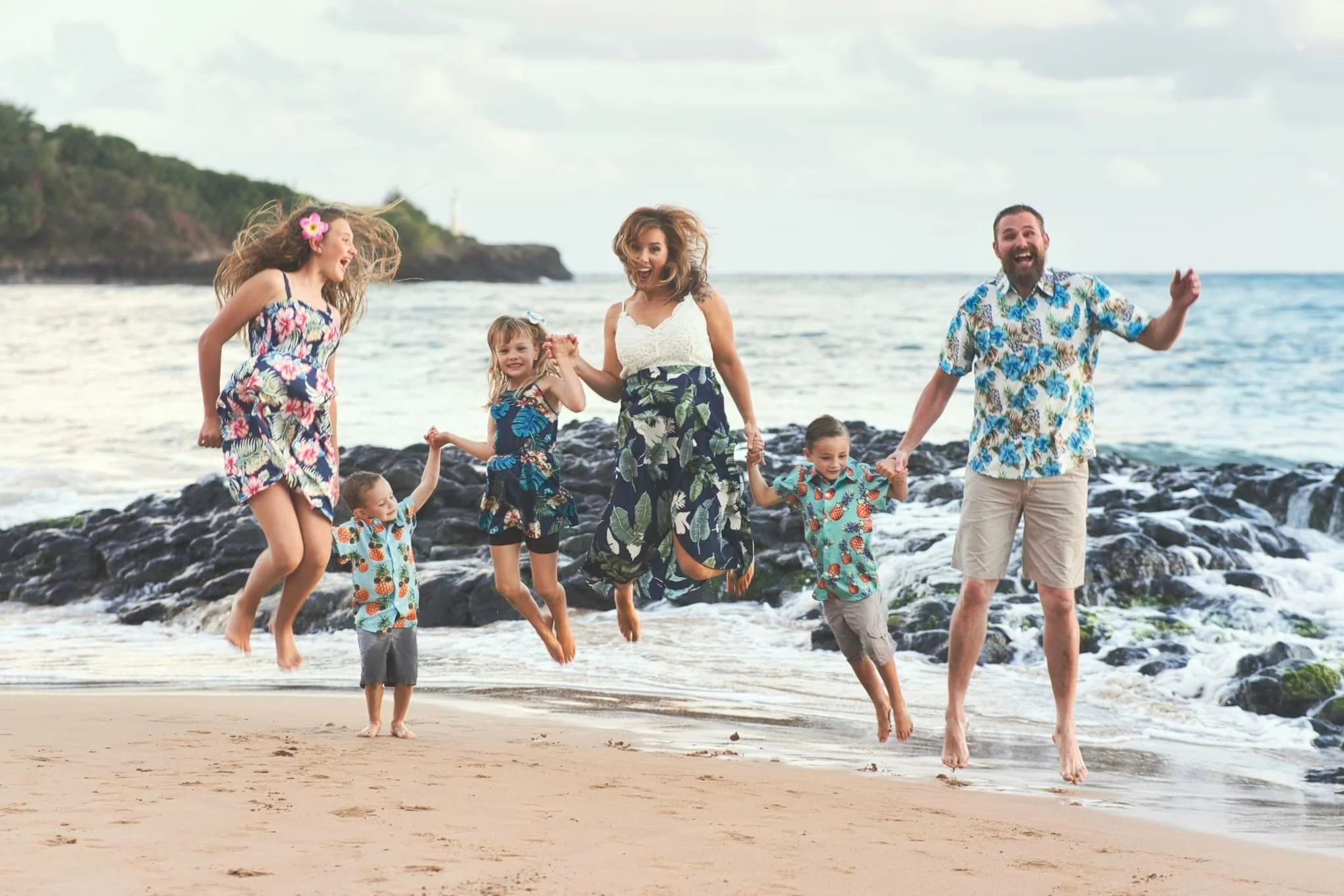 Family of six jumping for joy together on a rocky Kauai beach.