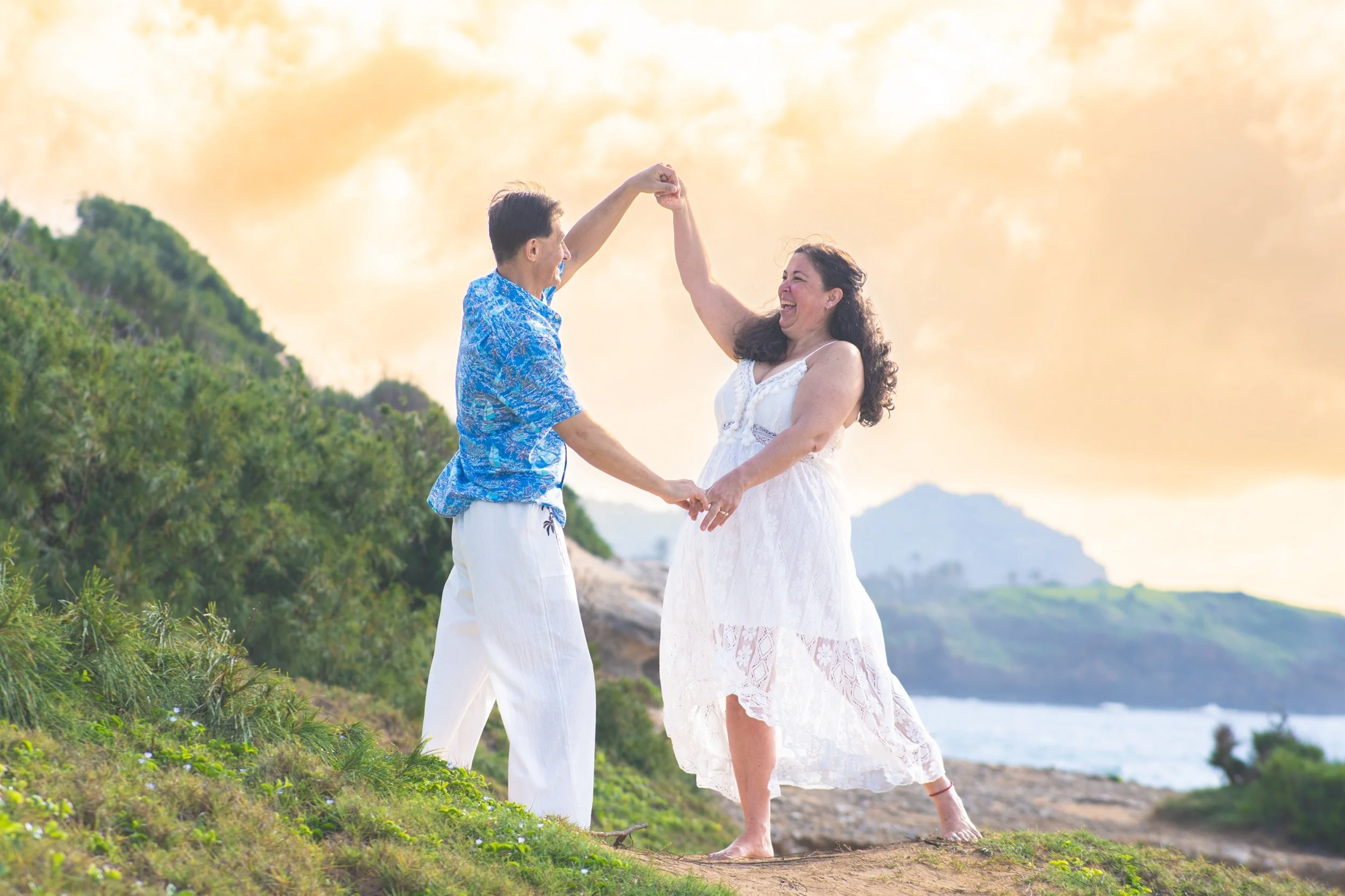 Couple dancing on a grassy hilltop with the ocean behind them in Kauai.