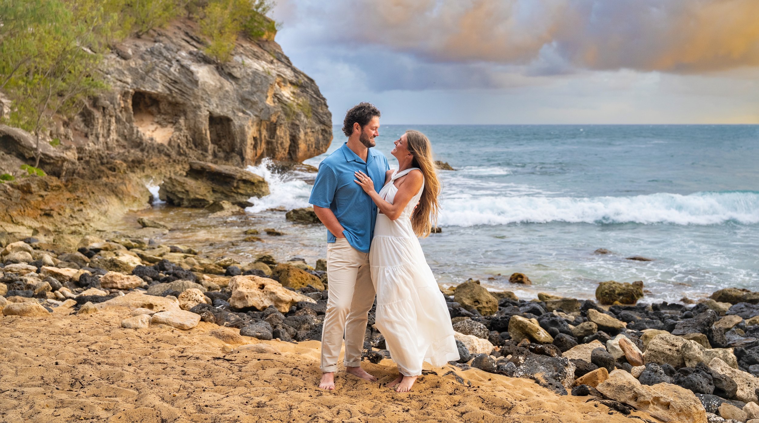 Couple embracing in a sandy cove at Shipwreck Beach, Kauai.