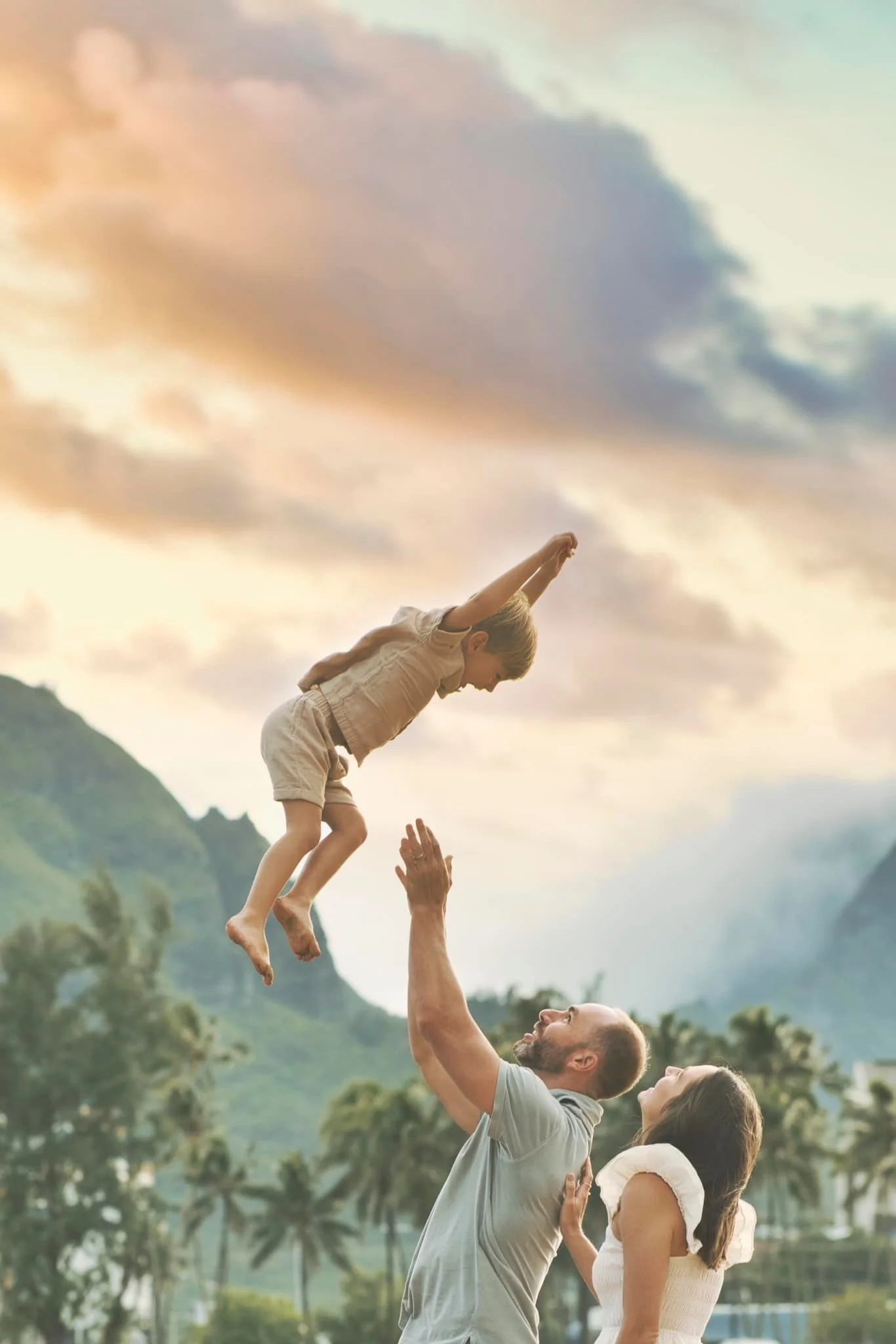 Dad playfully tossing his young son into the air at sunset on a Kauai beach.