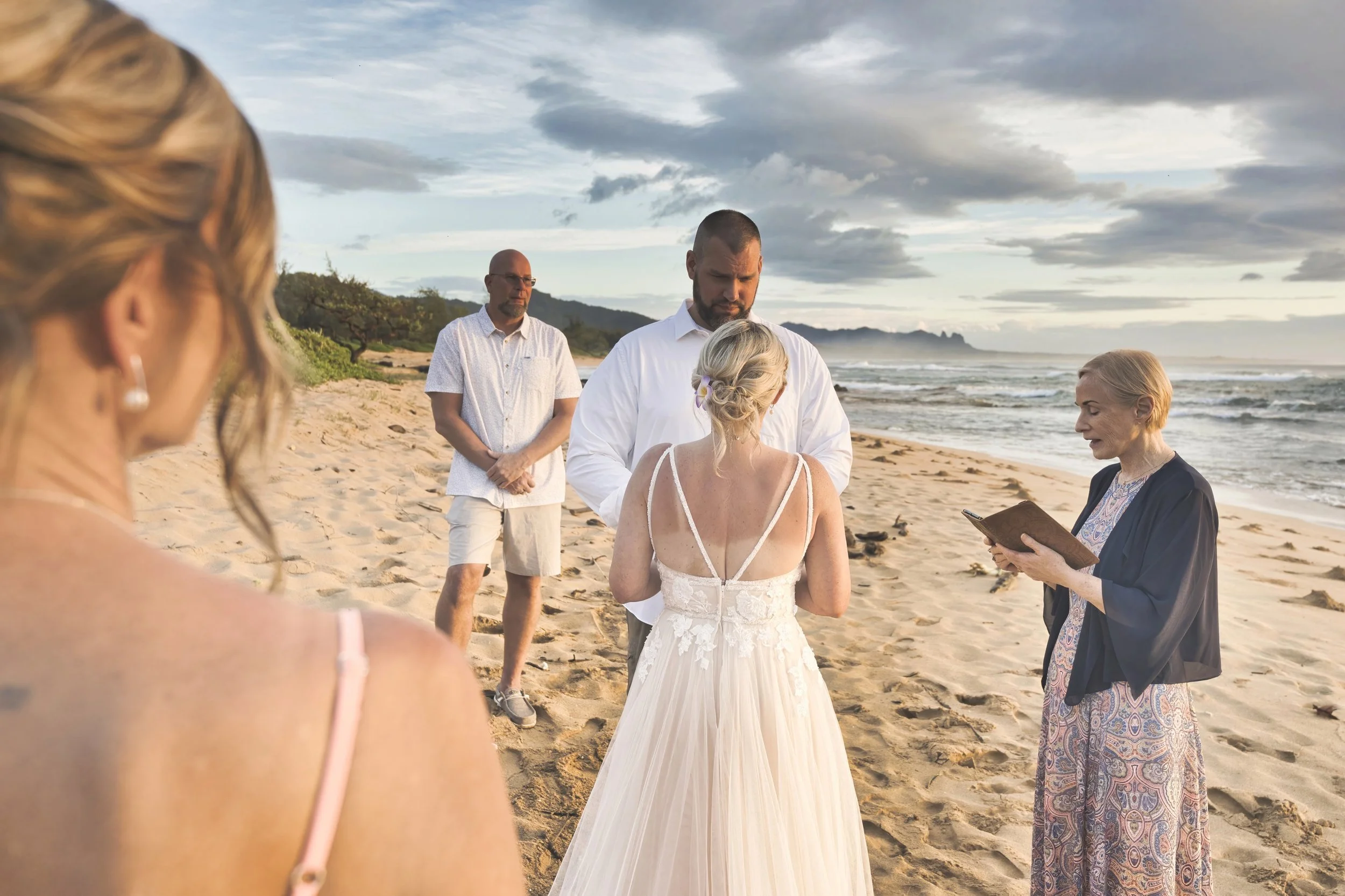 Bride and groom holding hands during their beach wedding ceremony in Kauai with the ocean behind them.