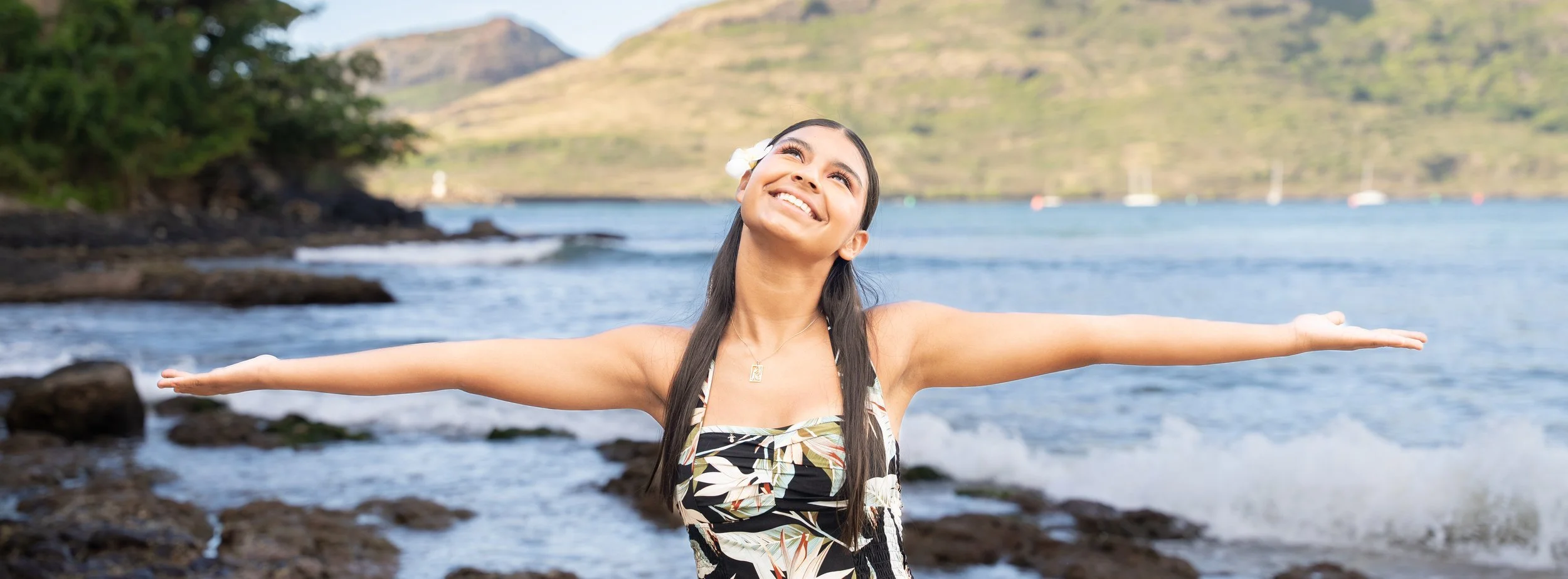 Young woman with arms outstretched smiling at the sky on a Kauai beach.