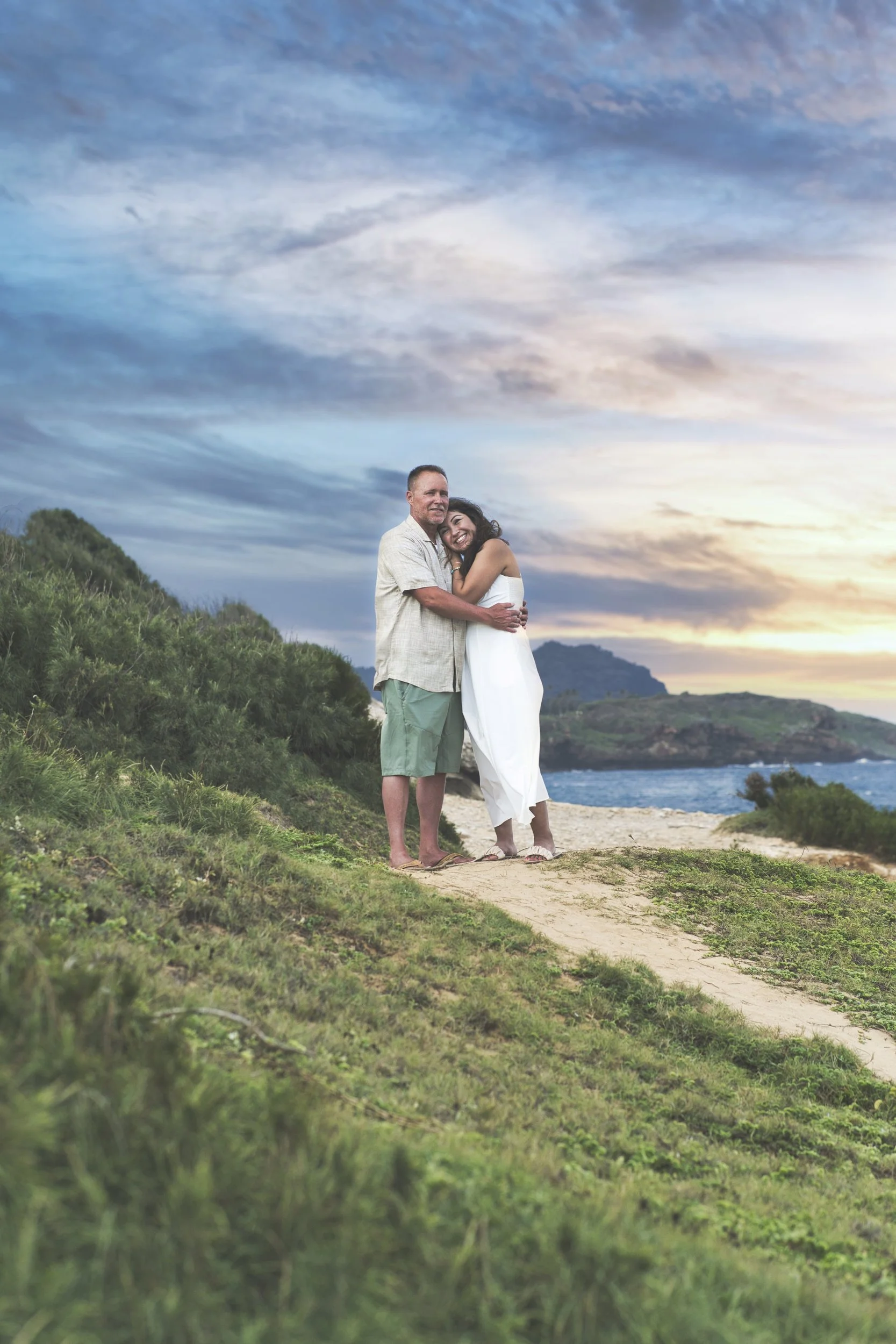 Couple embracing on a hilltop overlooking the ocean in Kauai at sunset.