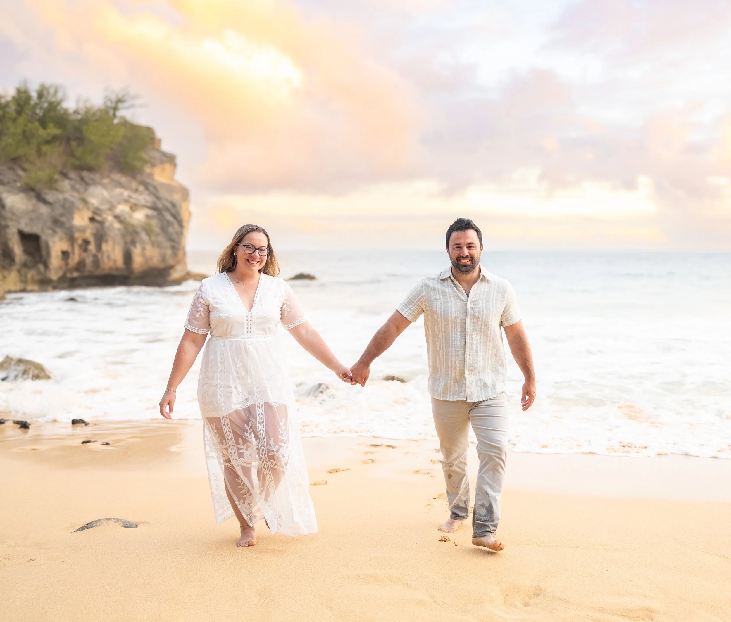 Smiling couple walking hand in hand toward the camera on a Kauai beach.