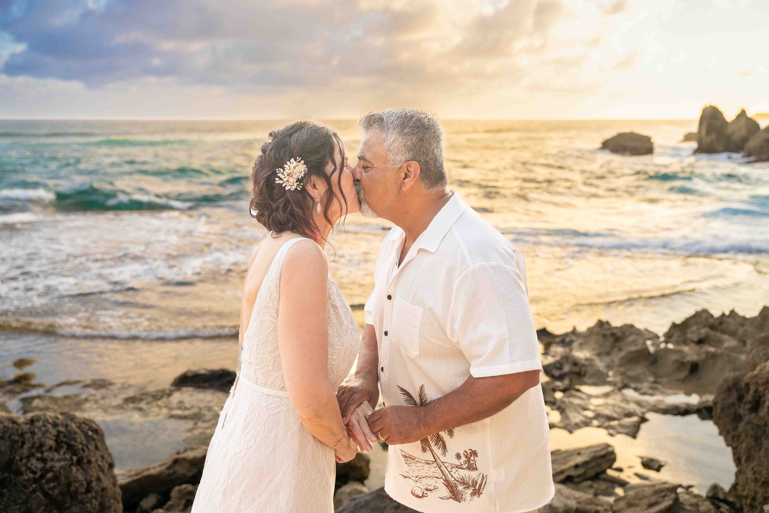 Older couple kissing on the rocky beach at sunset at Shipwreck Beach, Kauai.