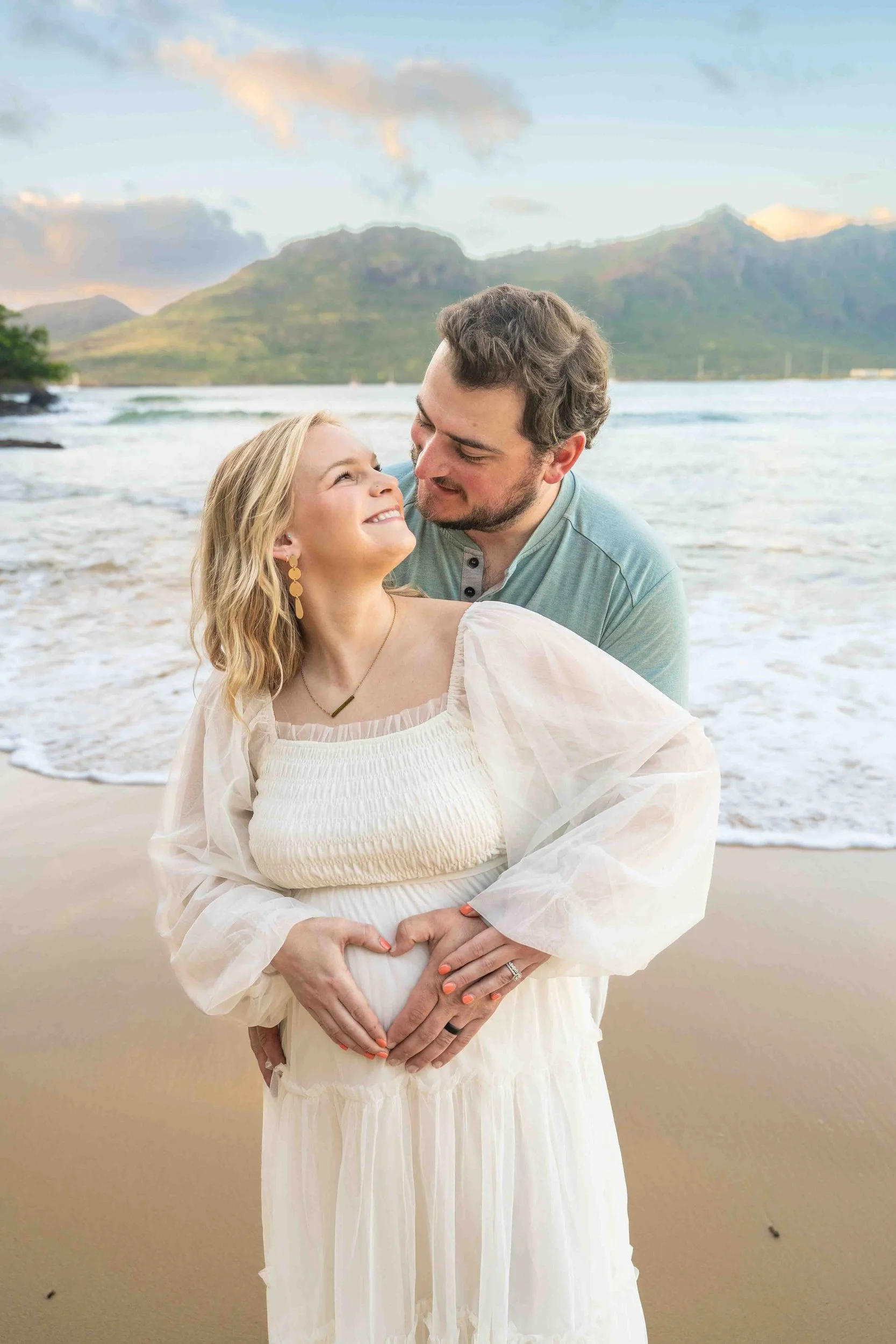 Couple forming a heart with their hands on the baby bump at a Kauai beach.