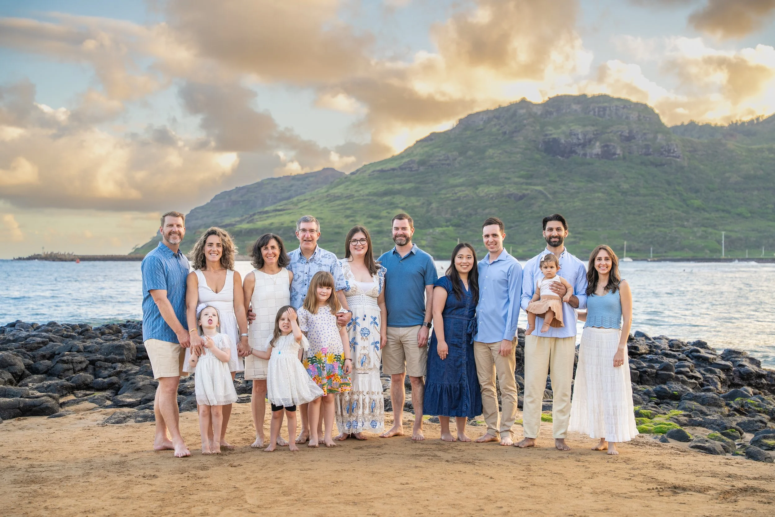 Large extended family posing on a Kauai beach at sunset with mountains behind them.