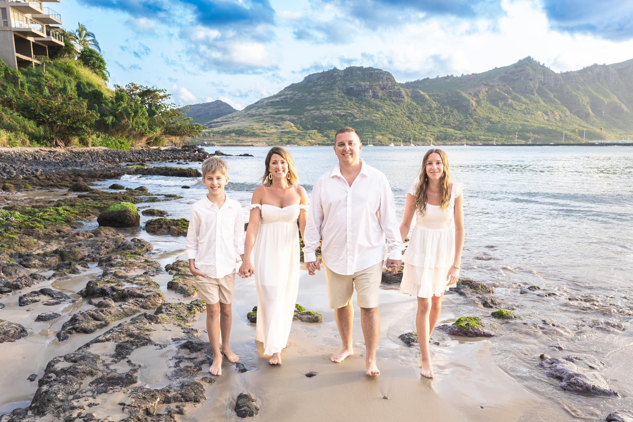 Family of four walking toward the camera on a rocky Kauai shoreline.