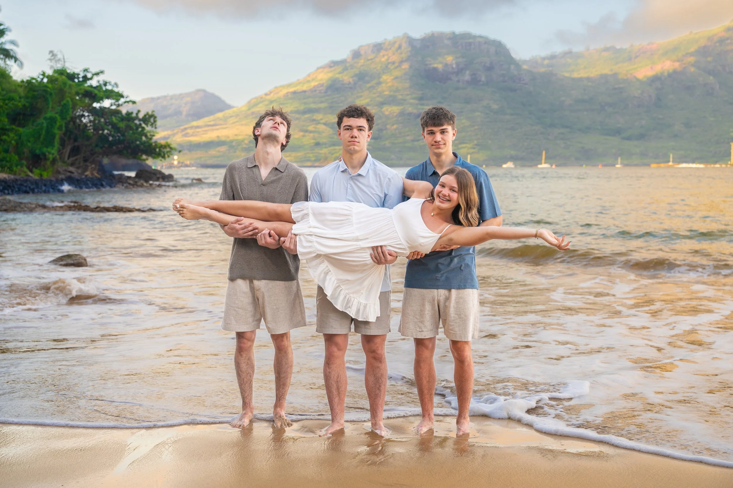 Three teenage boys playfully lifting their sister on a Kauai beach.