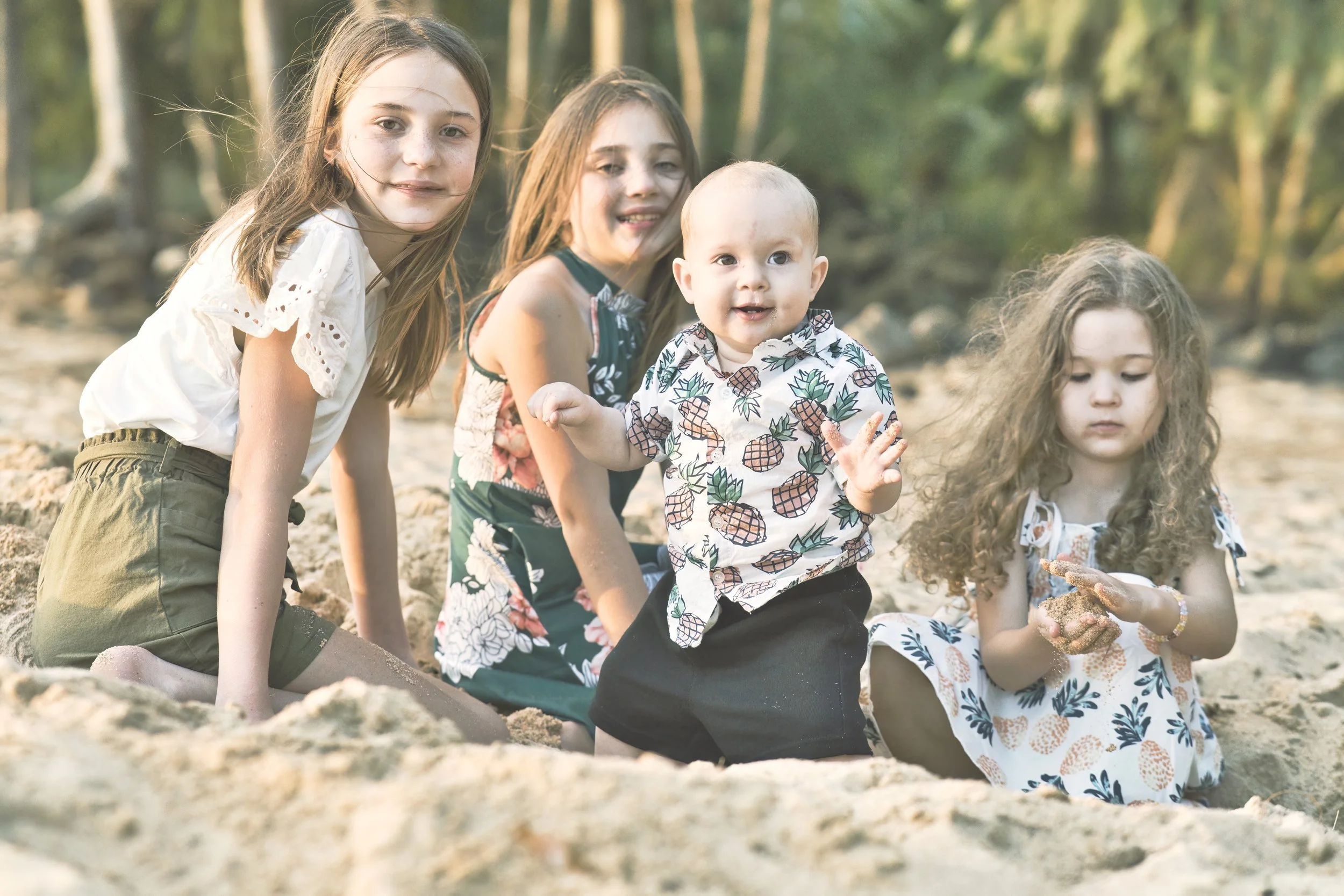 Four kids playing in the sand near the trees on a Kauai beach.