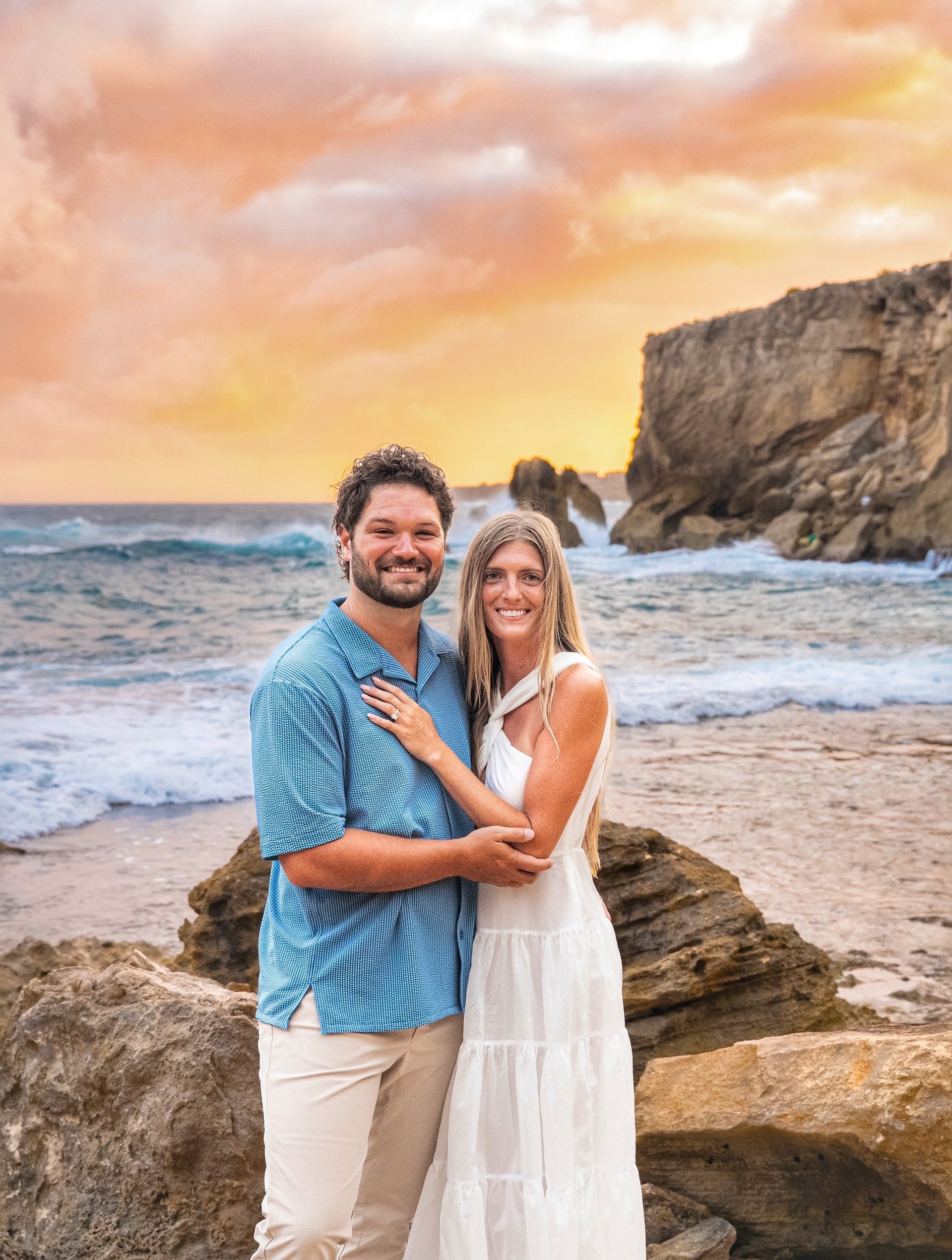 Smiling couple posing together on the rocks at Shipwreck Beach, Kauai, at sunset.