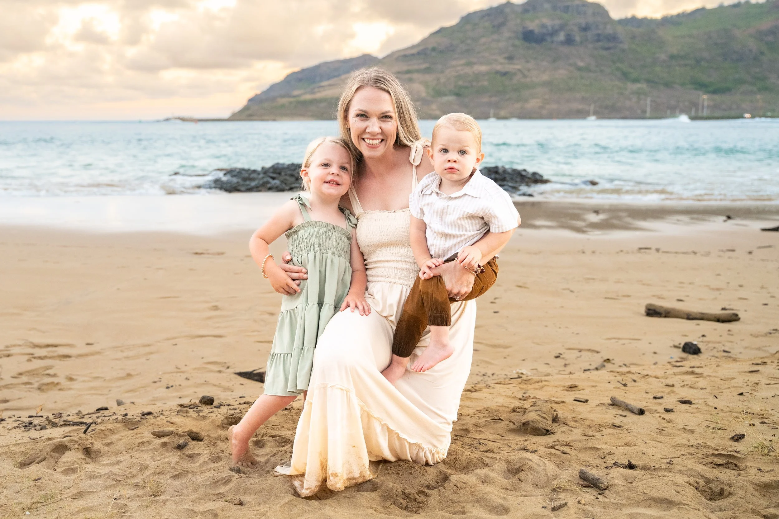 Mom kneeling on the sand with her daughter and toddler son on a Kauai beach.