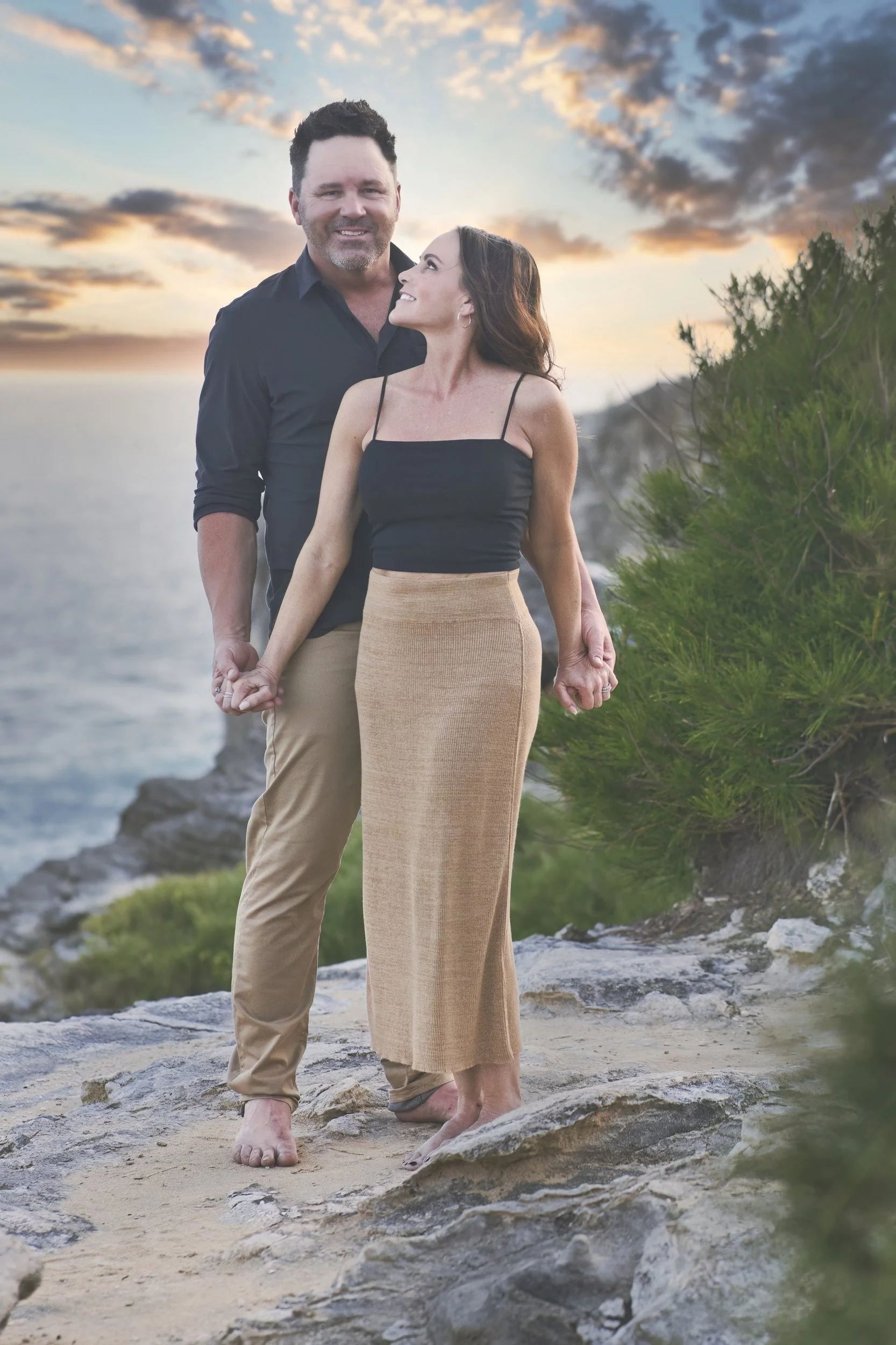 Couple holding hands on a cliff top at Shipwreck Beach, Kauai, at sunset.