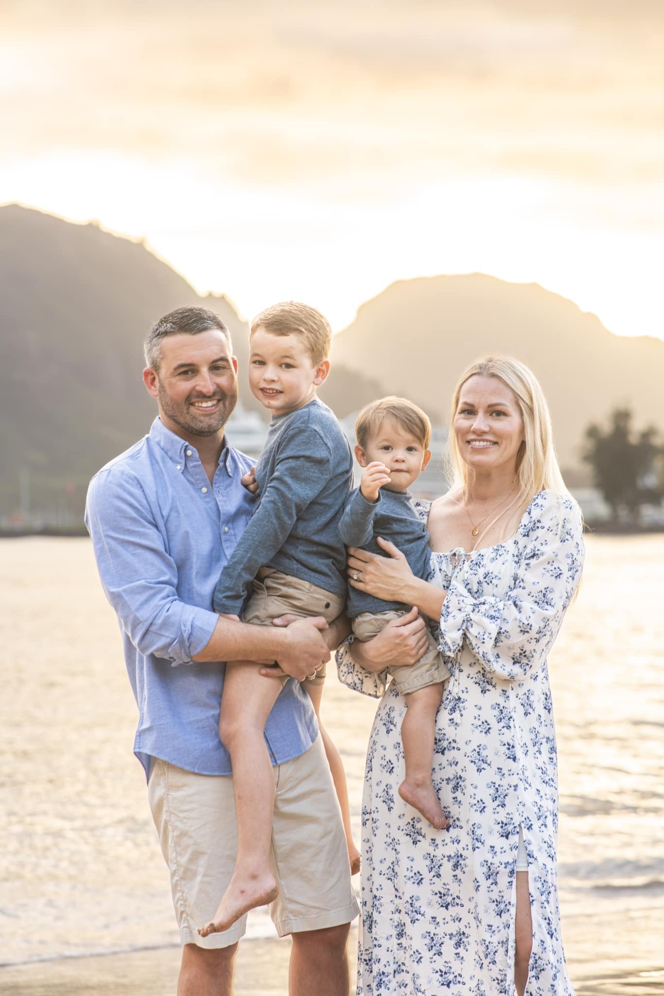 Family of four smiling together on a Kauai beach at sunset.