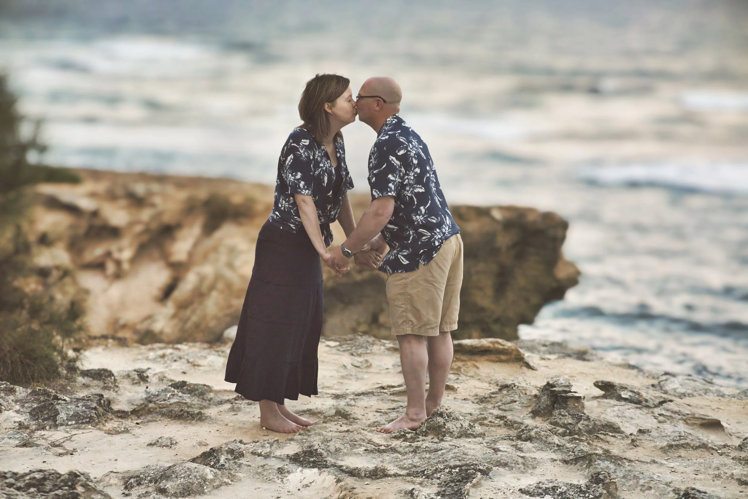 Couple kissing on the rocky shore as waves roll in at Shipwreck Beach, Kauai.