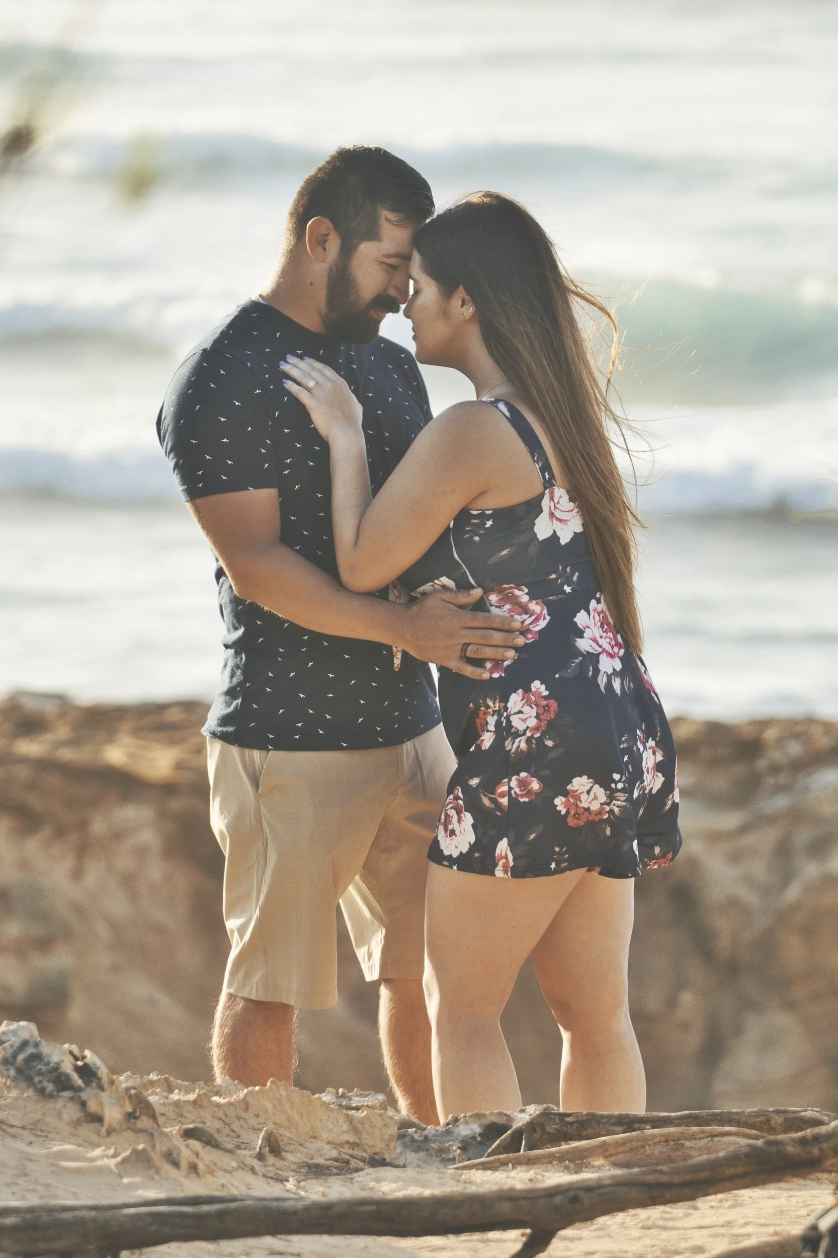 Couple embracing forehead to forehead on the rocky shore at Shipwreck Beach, Kauai.