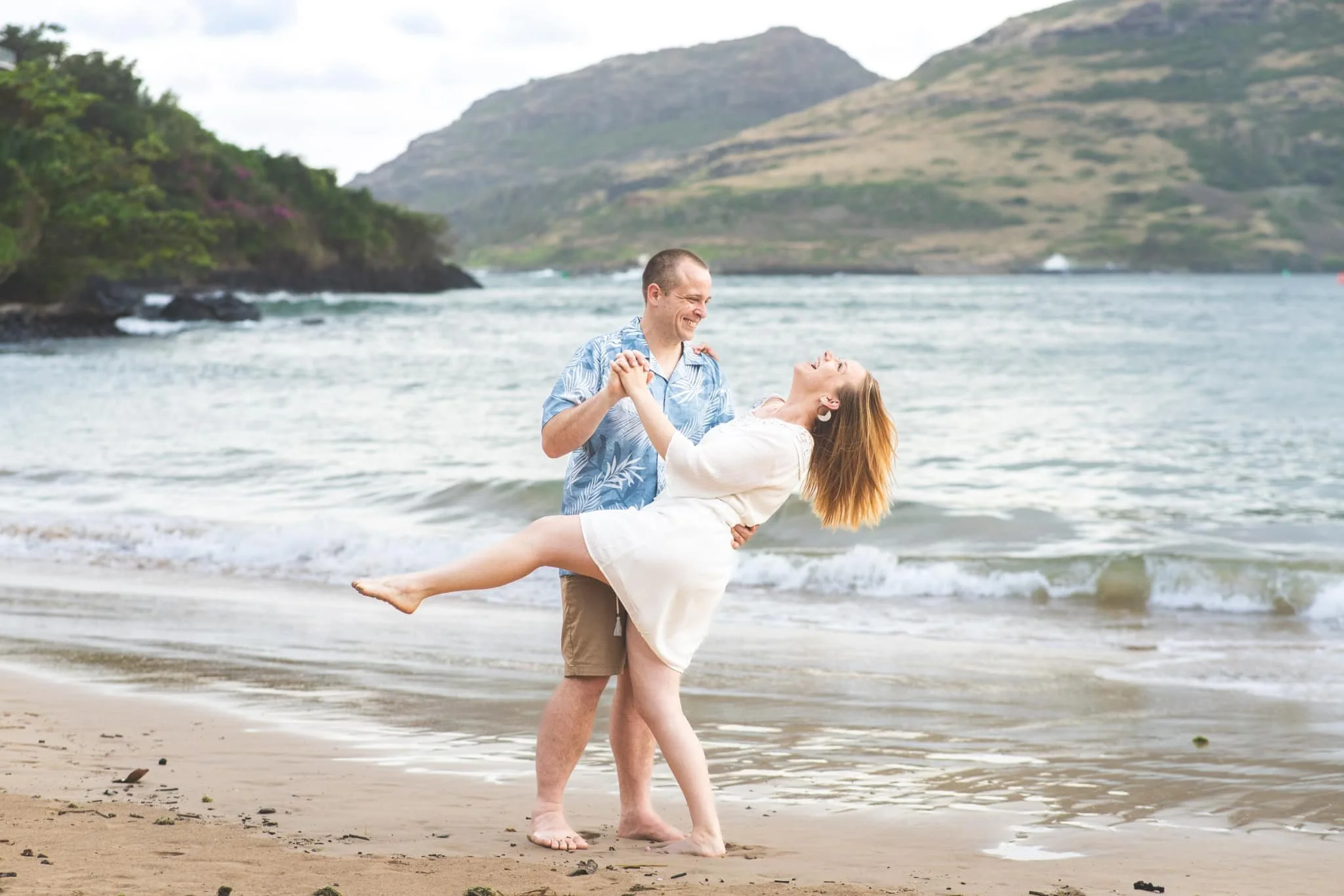 Man dipping his partner while dancing and laughing on a Kauai beach.