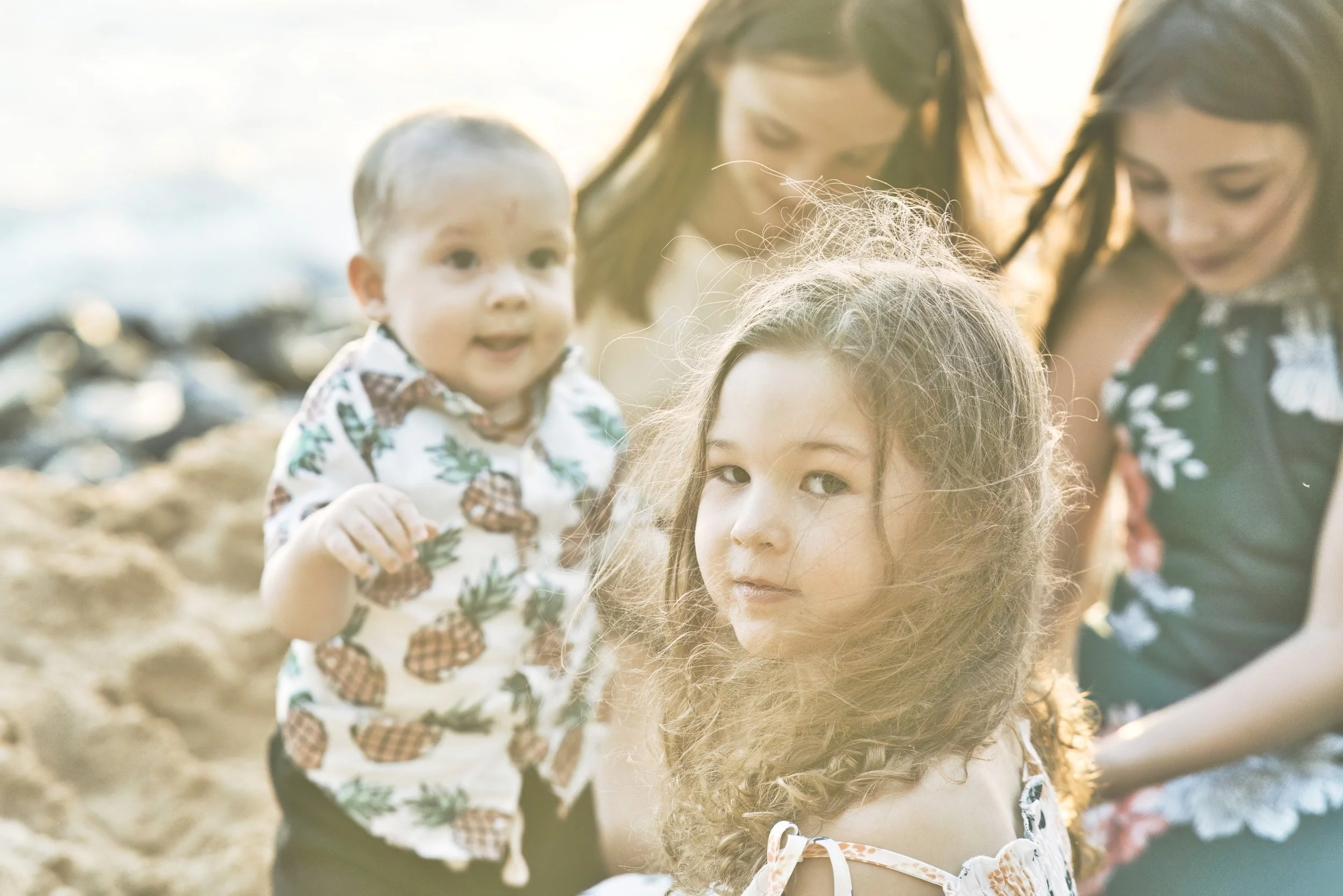 Close-up portrait of three kids smiling on a Kauai beach with the ocean behind them.
