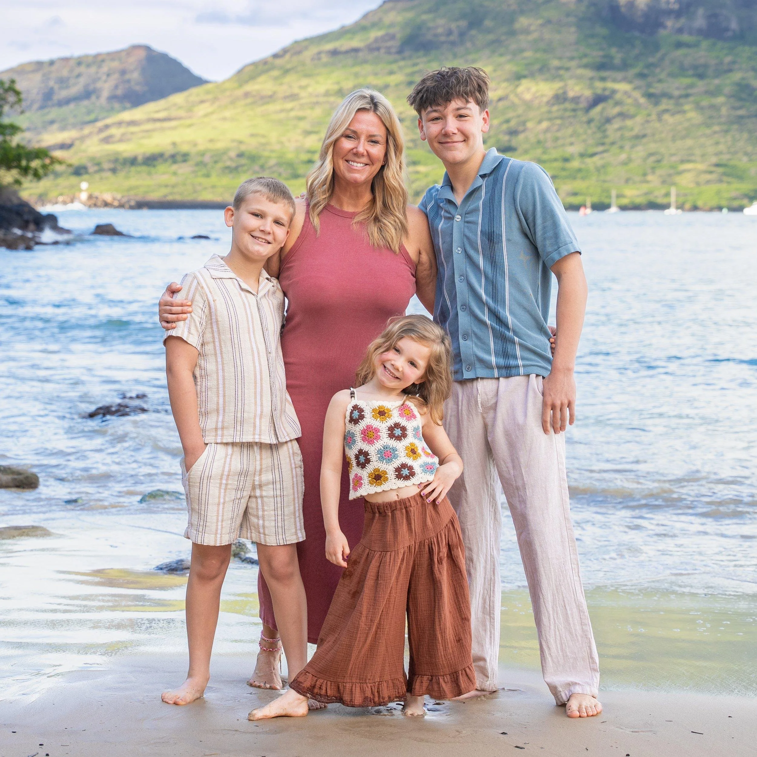 Mom with her three kids smiling at the water's edge on a Kauai beach.