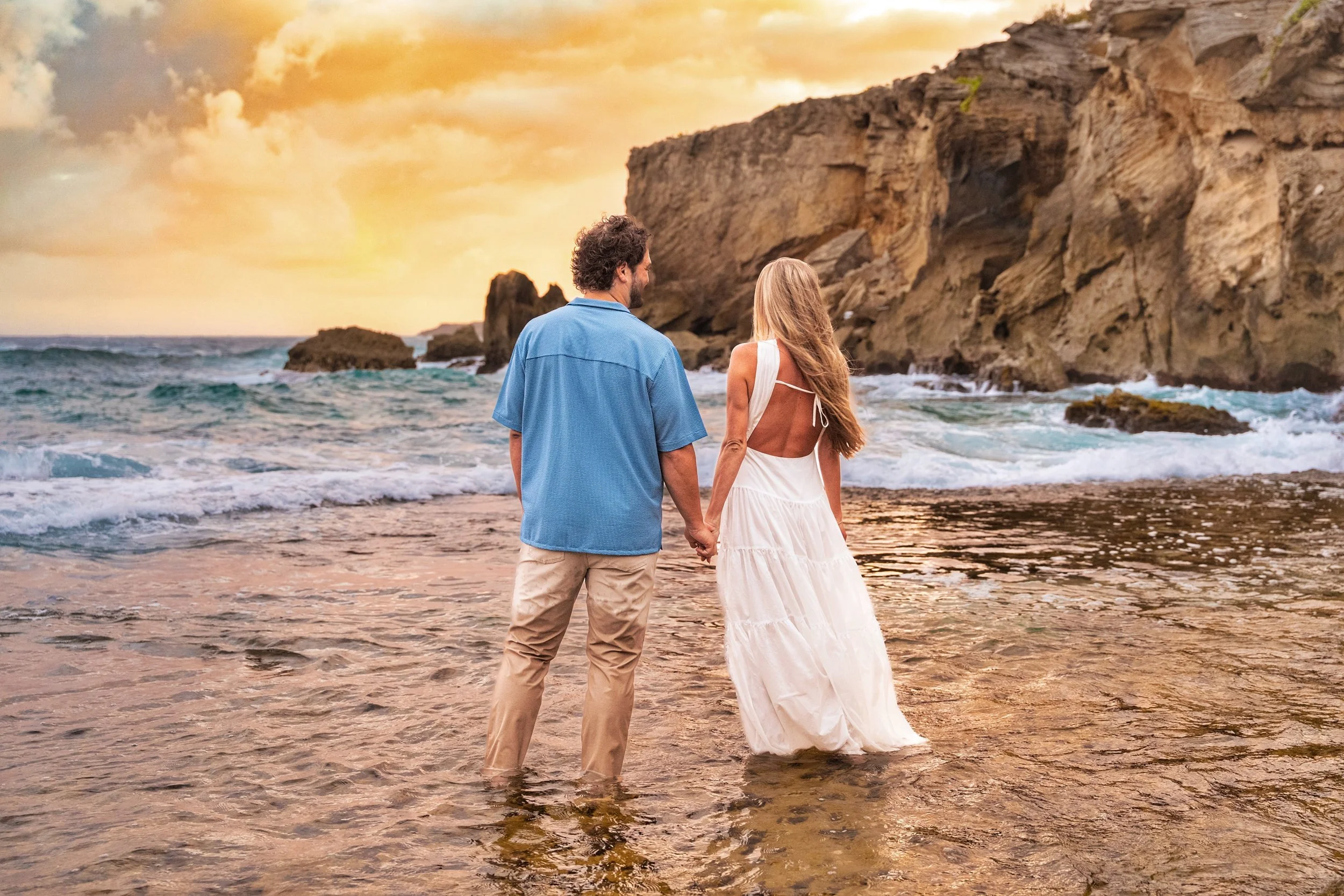 Couple holding hands walking into the surf toward the cliffs at Shipwreck Beach, Kauai.